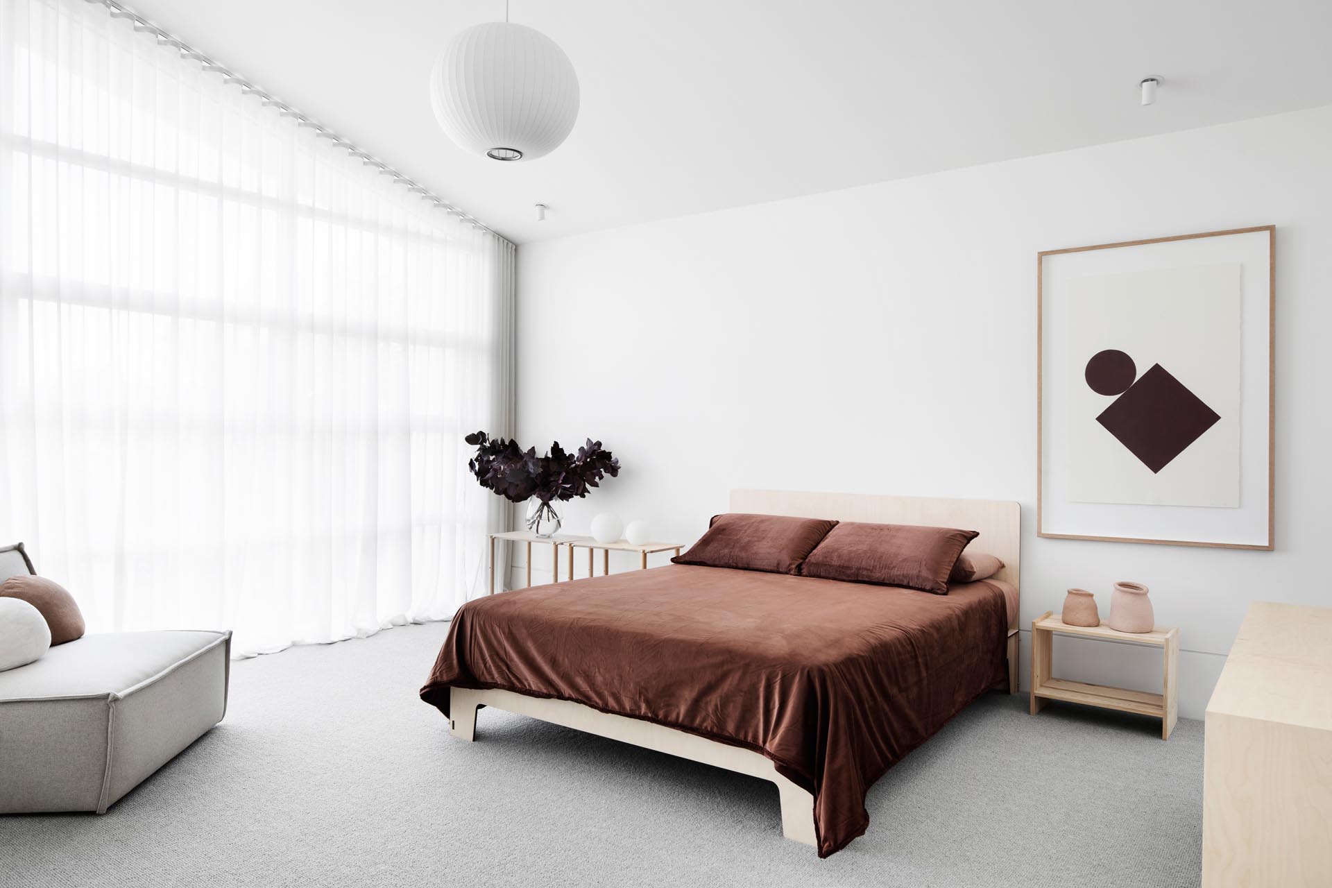 In this master bedroom, the dark brown bedding contrasts with the lighter elements in the room, like the flooring, bedside tables, and upholstered chair.