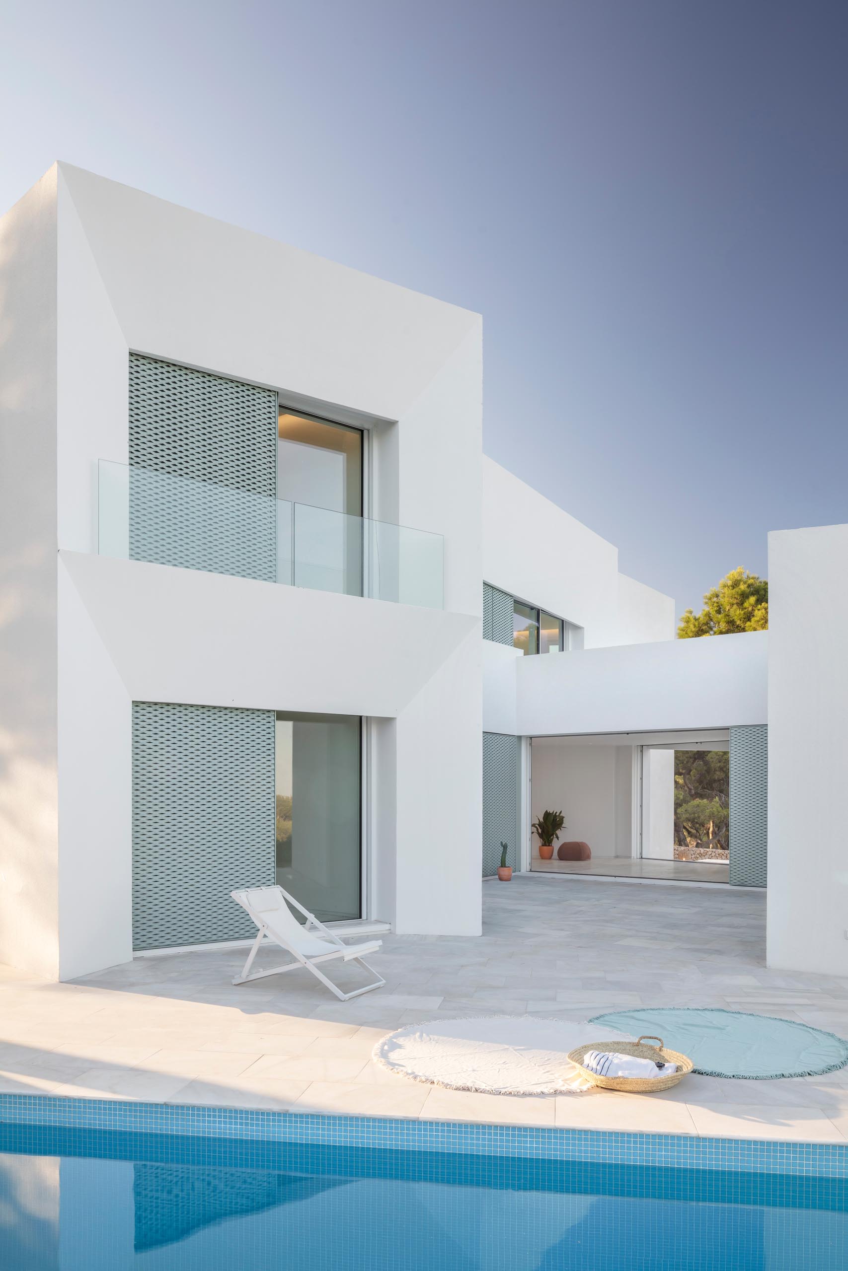 A modern white home with pastel turquoise perforated aluminum screens, a patio, and swimming pool.