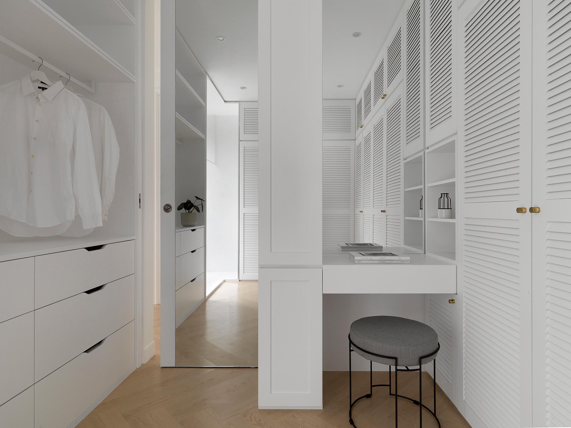 A modern walk-in closet designed with white cabinets, a small vanity, and floor-to-ceiling mirror behind the door.