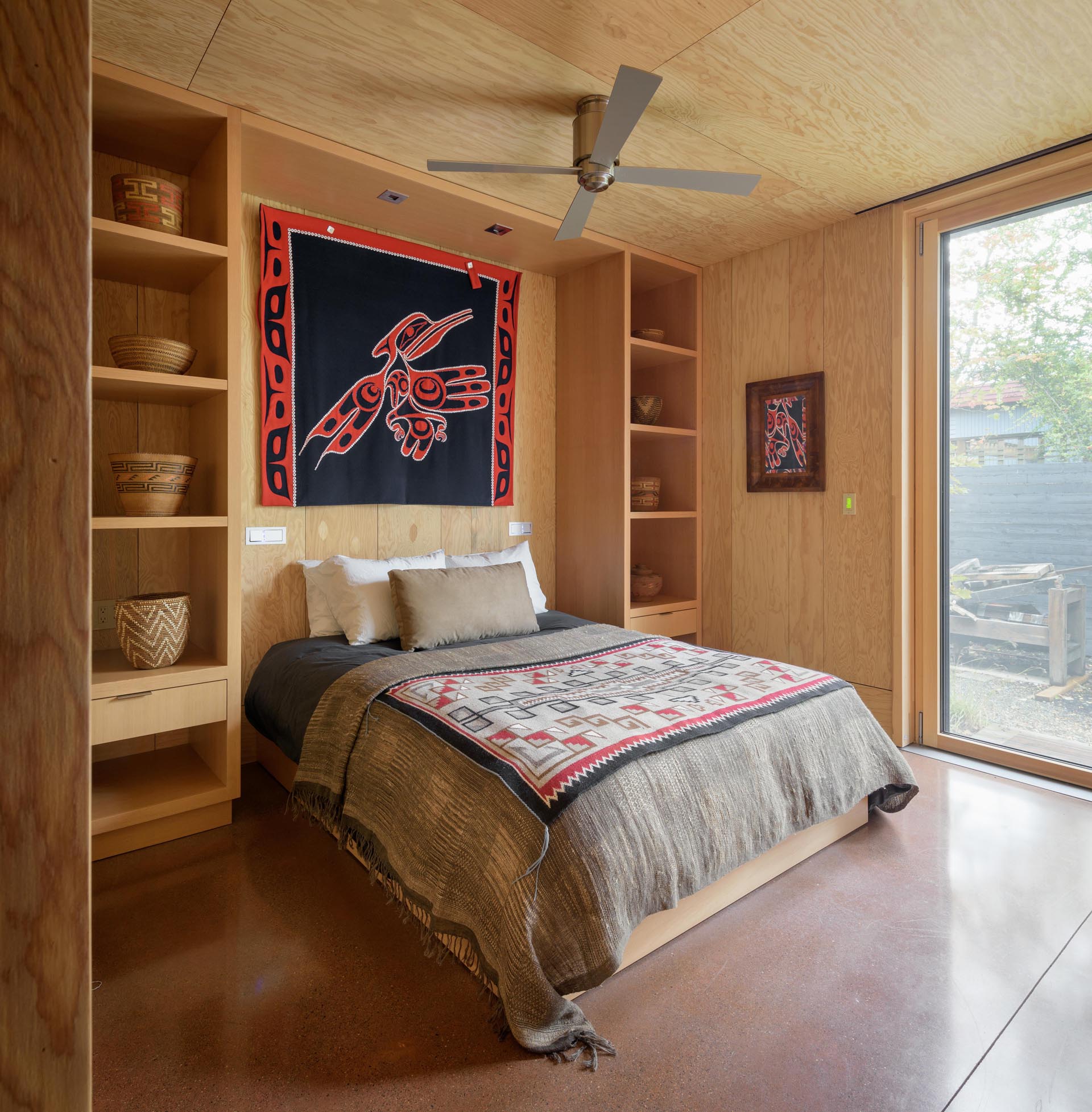 A contemporary cabin bedroom with concrete floors and built-in shelving.