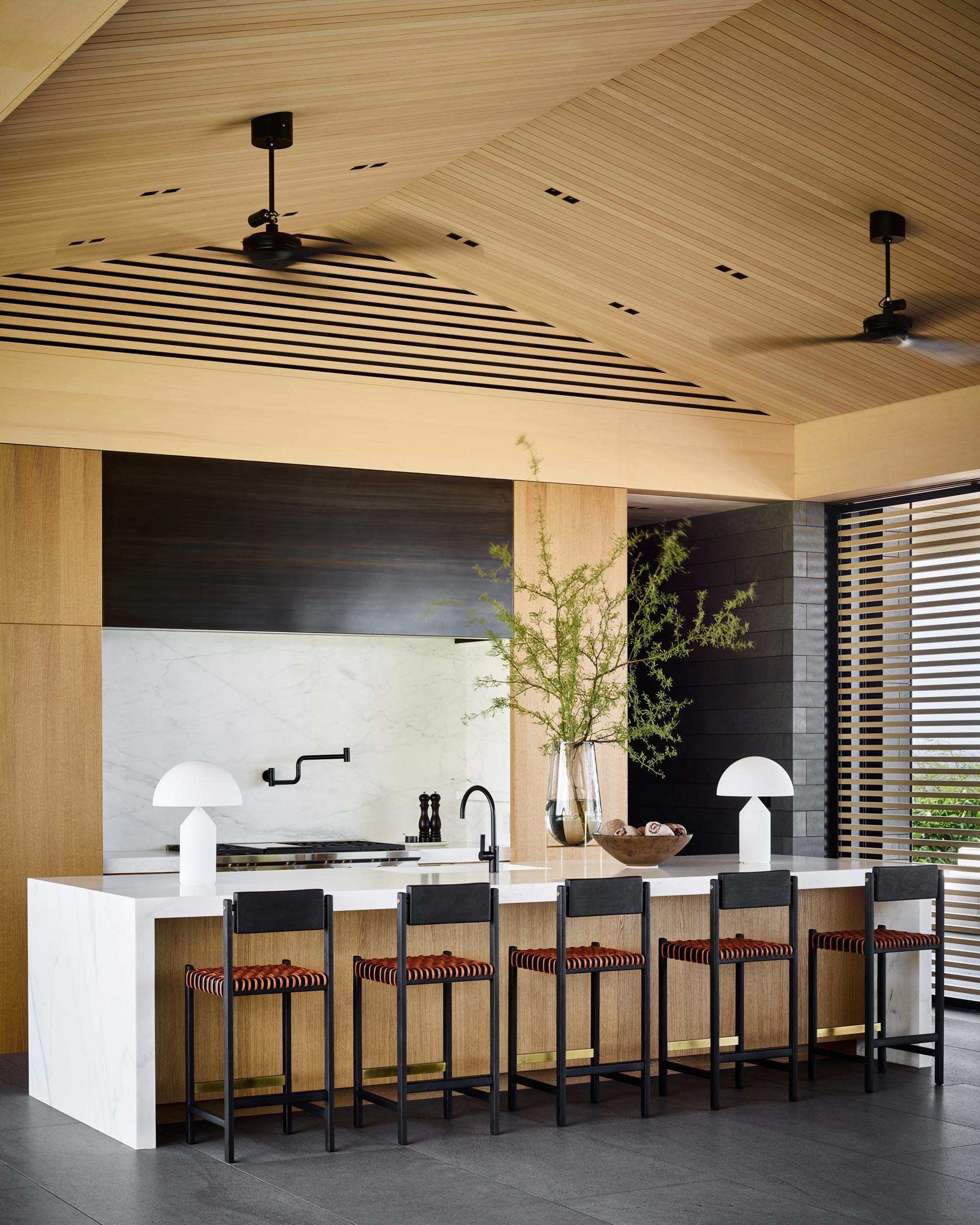 This modern kitchen includes a large island with room for seating and a waterfall countertop. Behind the kitchen, there's a walk-through pantry with wood cabinets and open shelving.