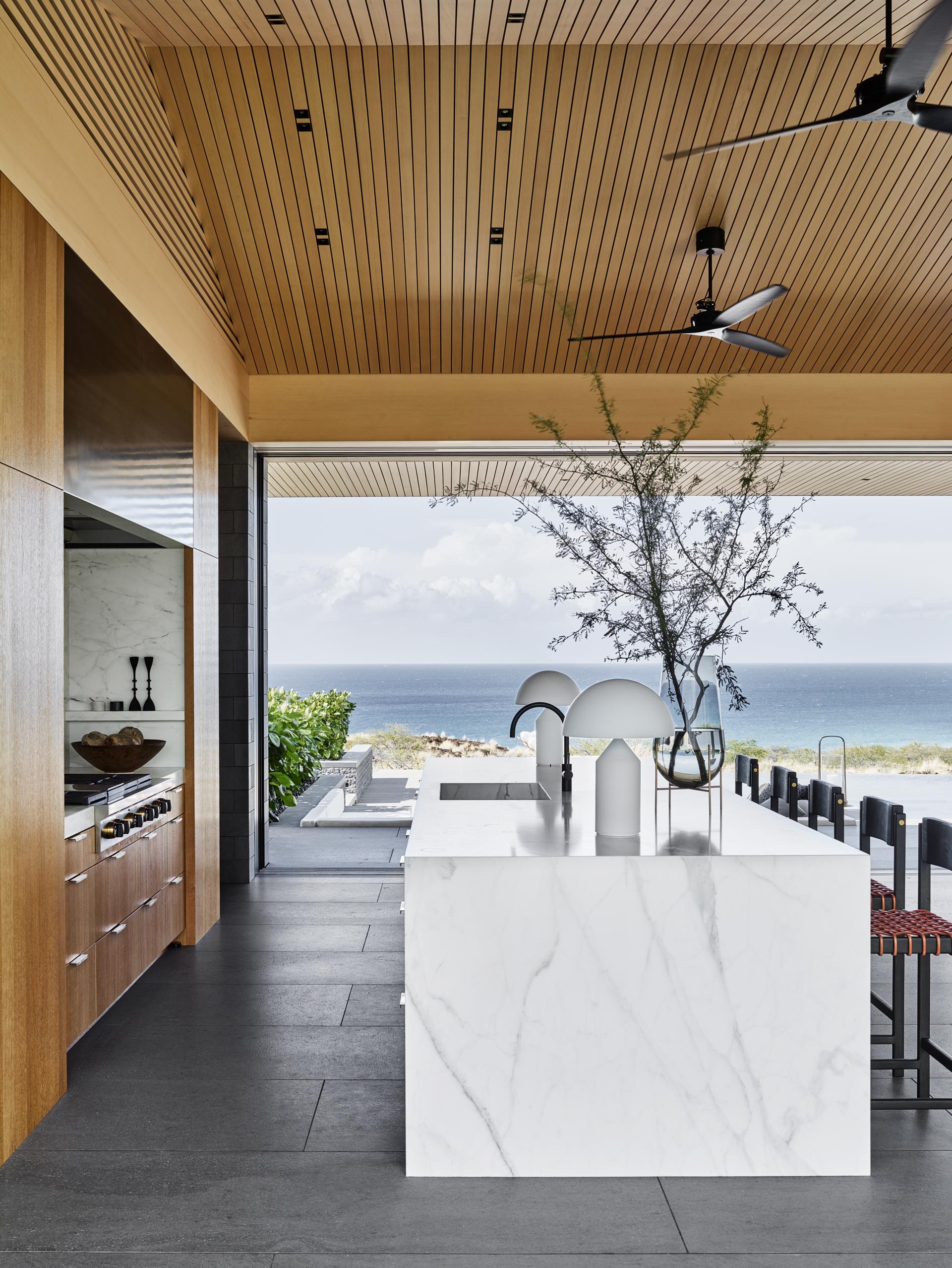 This modern kitchen includes a large island with room for seating and a waterfall countertop. Behind the kitchen, there's a walk-through pantry with wood cabinets and open shelving.