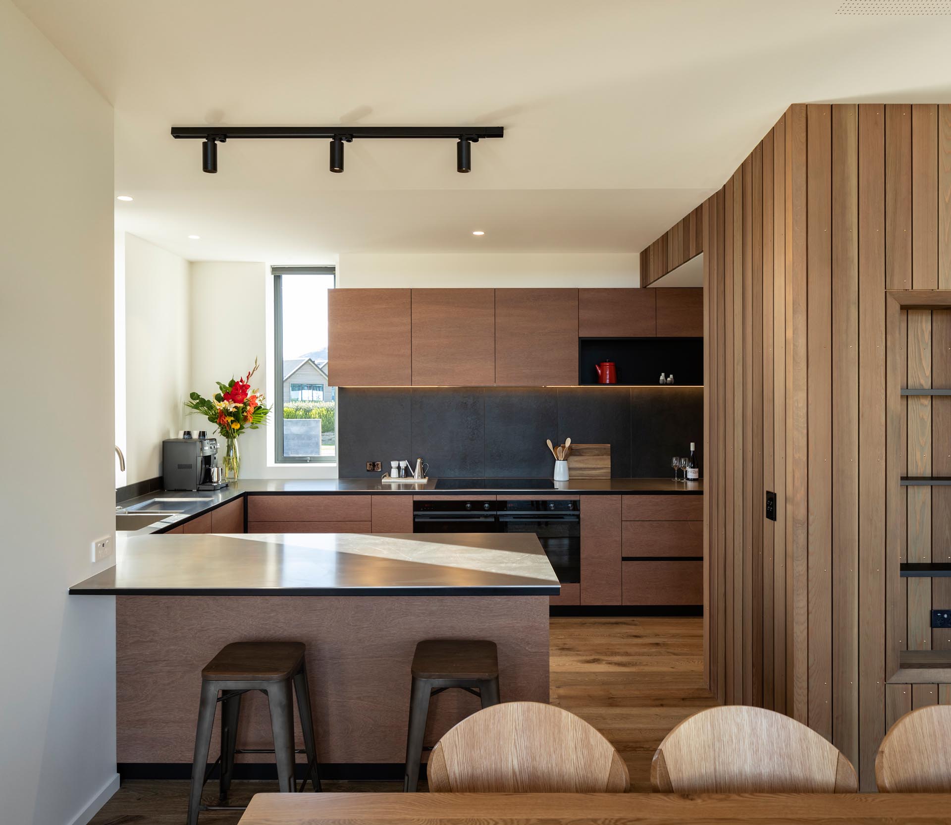 A modern kitchen with minimalist warm wood cabinets that have been paired with a gray backsplash and dark countertops for a contemporary look.
