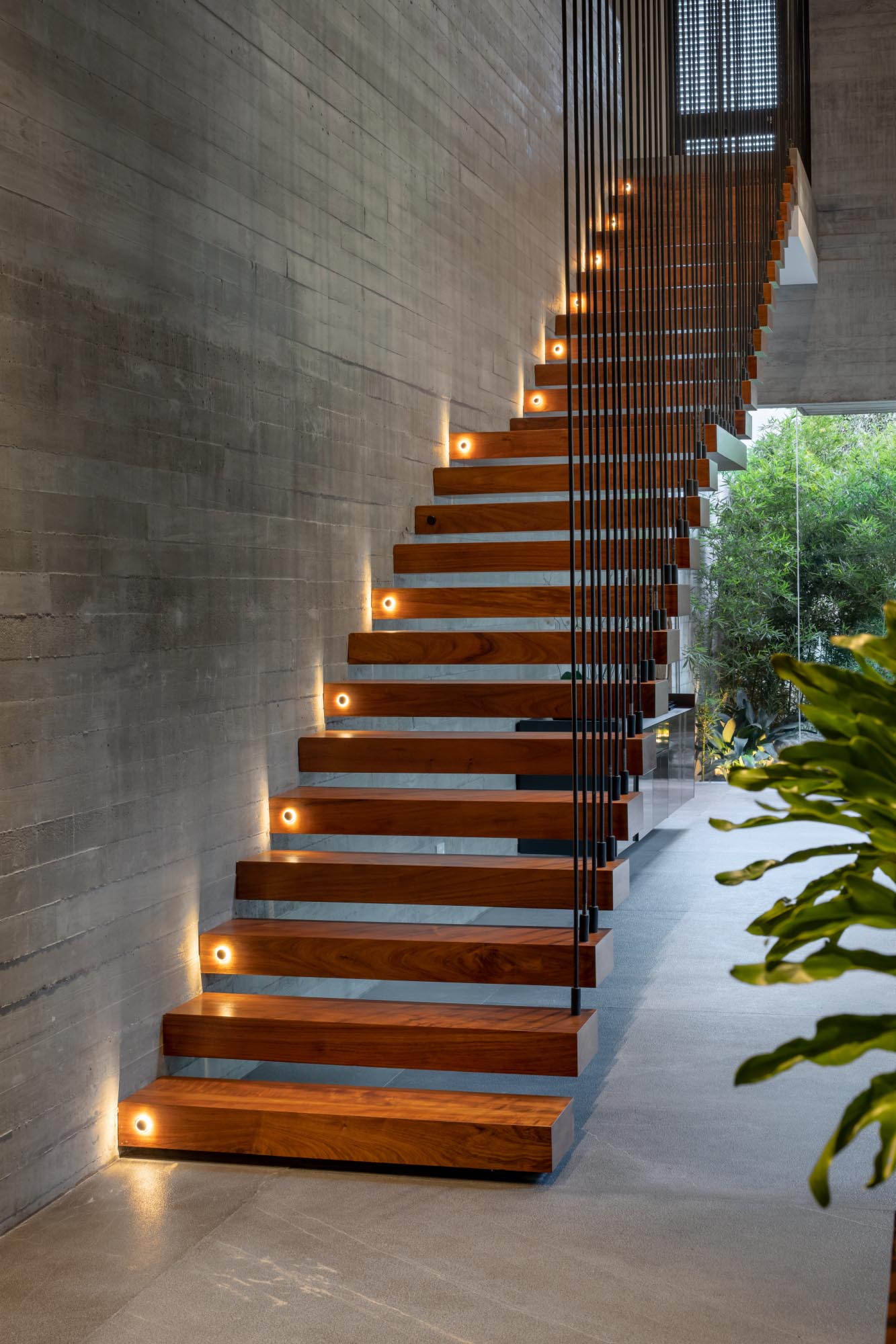A board-formed concrete wall is visible alongside a wood staircase, which also lights up at night.