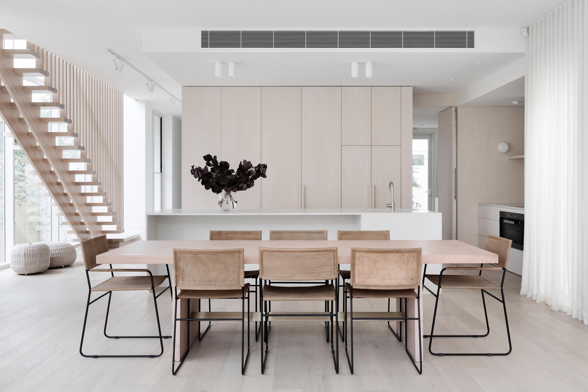 This modern house features a dining room with a light wood table, and a kitchen with minimalist cabinets and a white island.