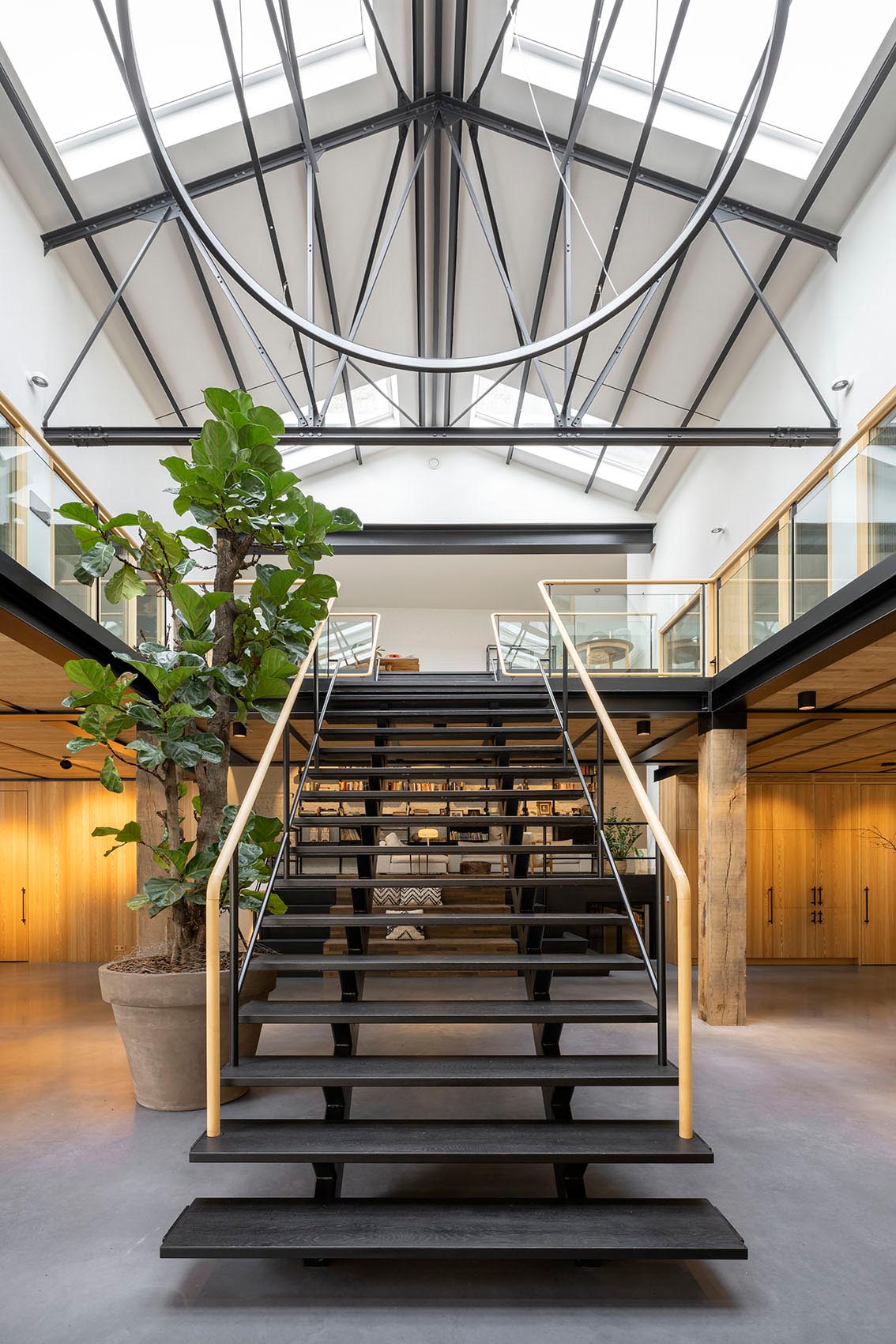 A remodeled gymnasium with a black staircase, 10 large skylights, black trusses, an open walkway and a large open plan main floor.