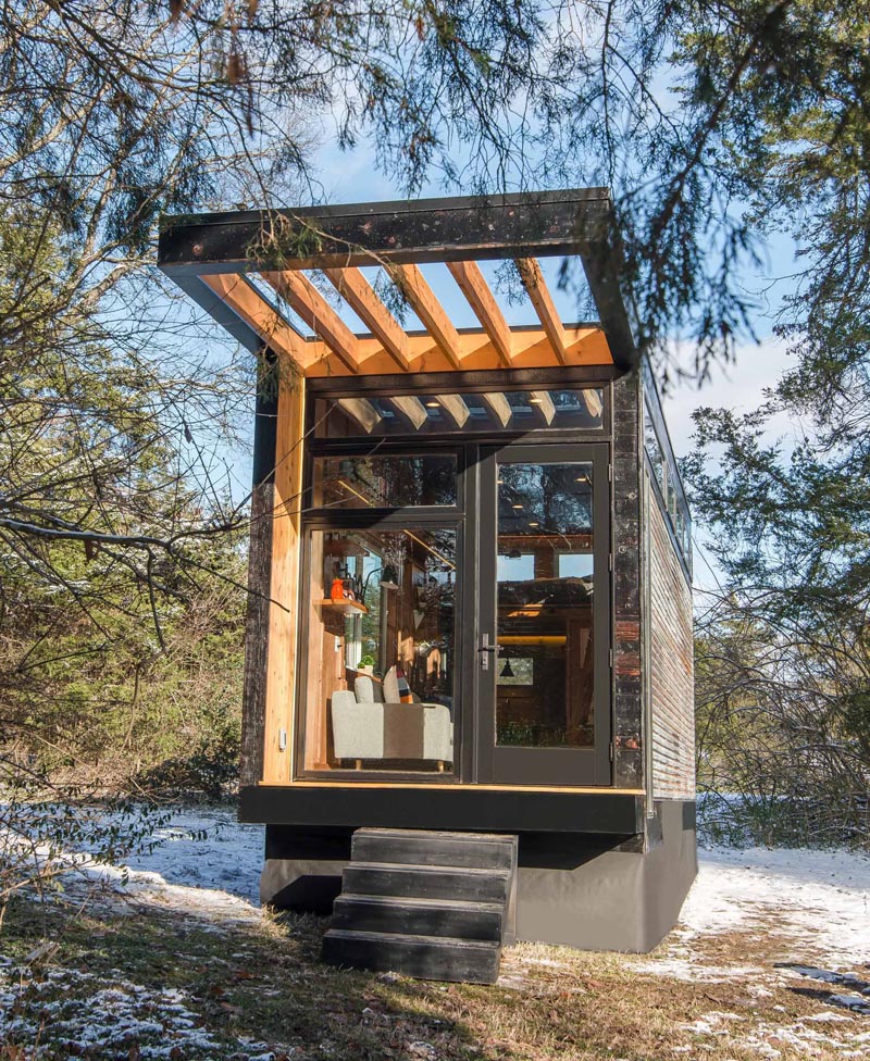 This modern tiny house has corrugated metal siding, shou sugi ban cedar trim, and a cedar cantilevered deck and pergola.
