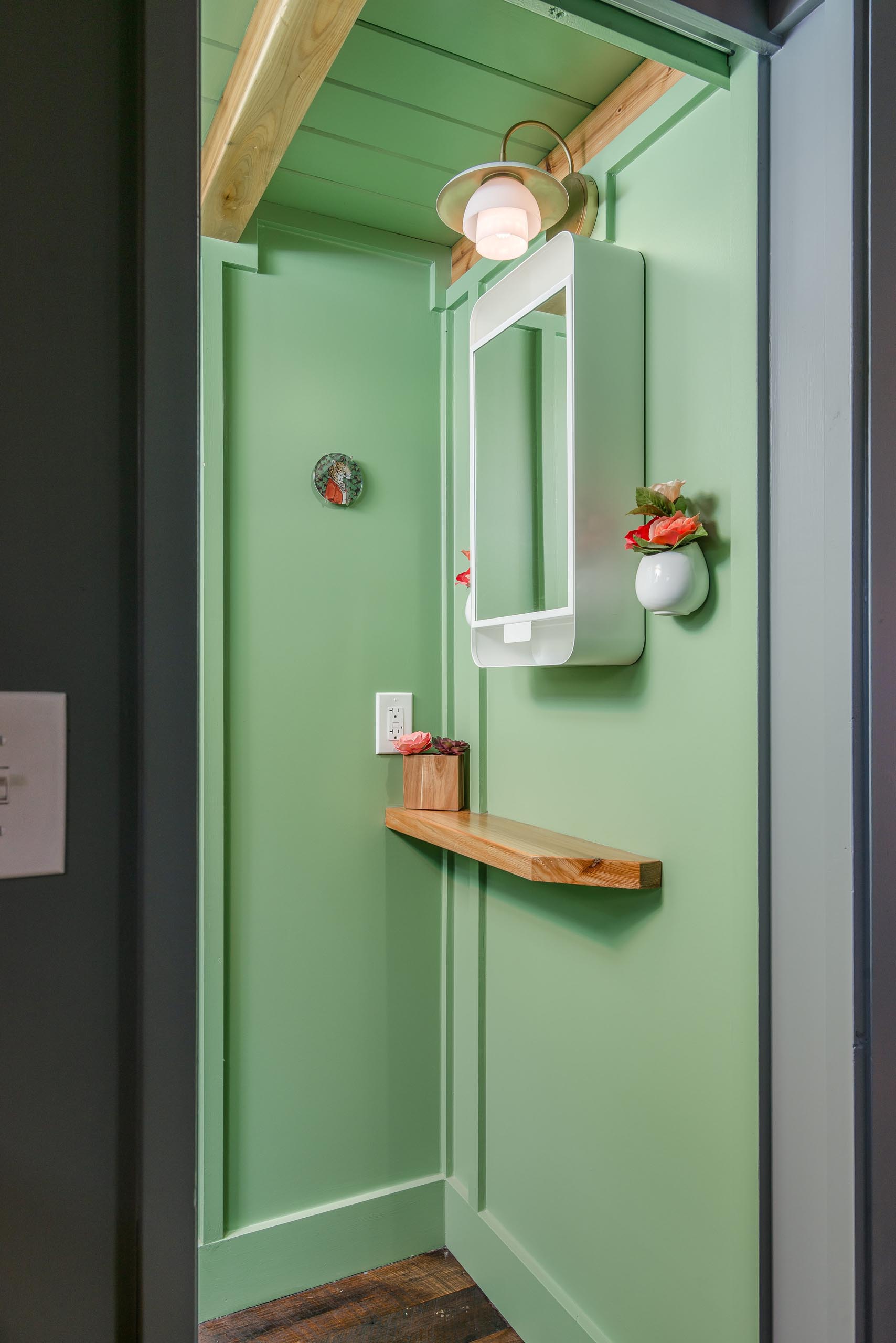 This tiny house bathroom hides behind a sliding pocket door and includes a pastel green finish, a waterless toilet, vanity area, and a shower.