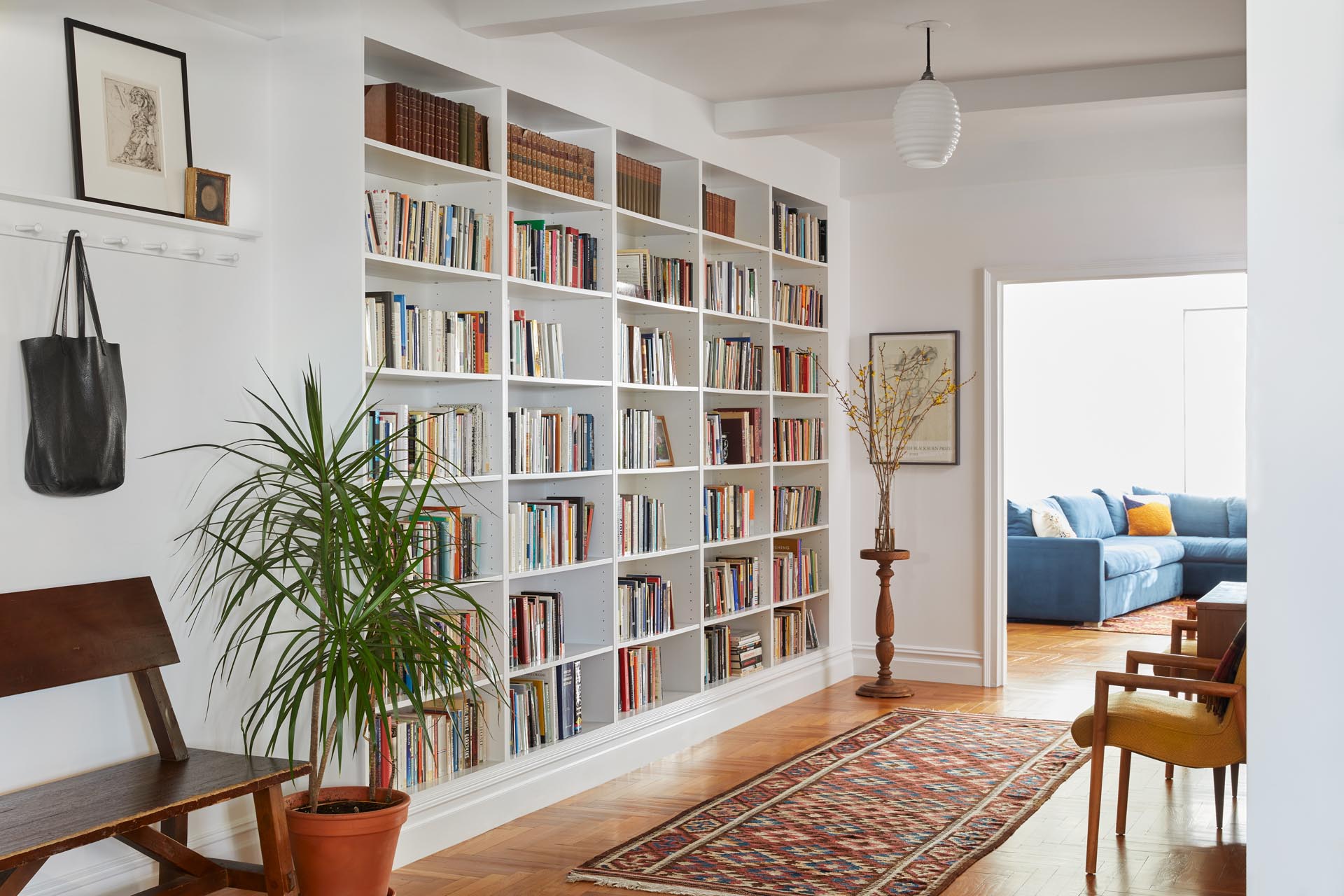 A remodeled entryway with a vintage German Opaline Glass Bauhaus lighting fixture, a Shaker-style hook/shelf system, and a floor-to-ceiling bookcase.