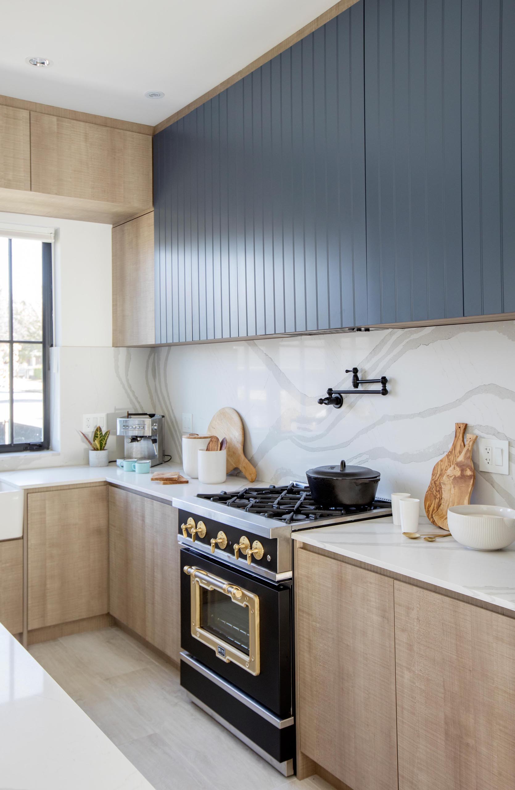 A modern kitchen with minimalist wood cabinets, light countertops, and black accent cabinets.