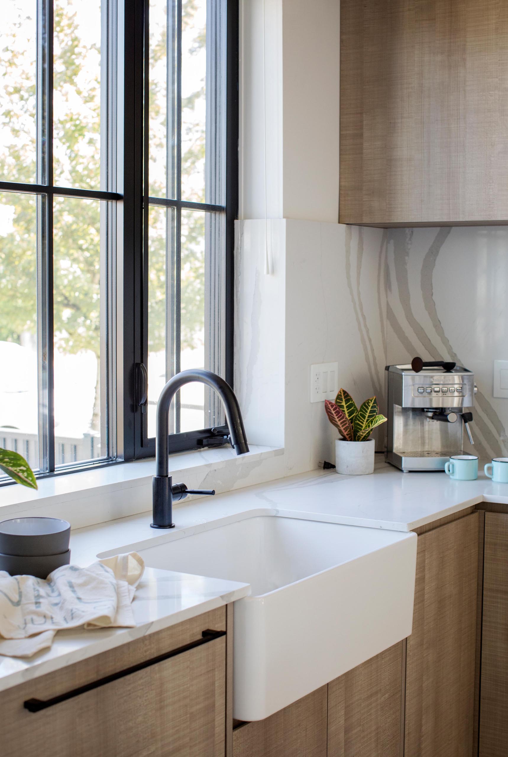 A modern kitchen with an apron front sink, light countertops, and wood cabinets.