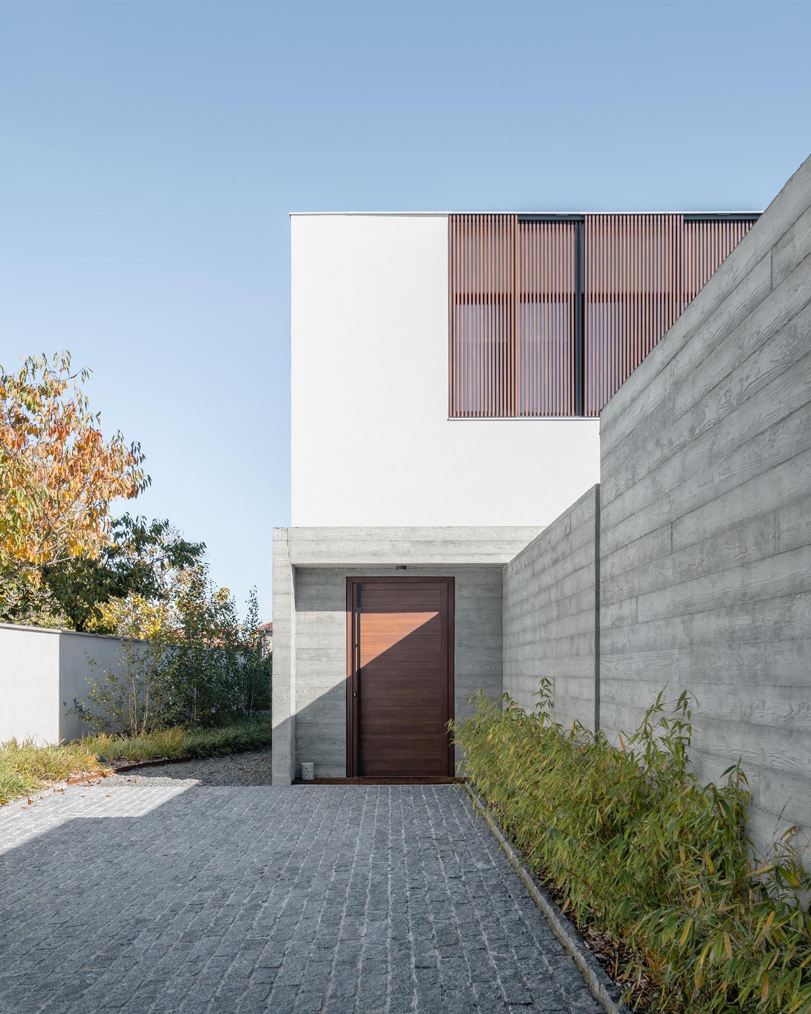 A small driveway with a concrete wall and plants, and a wood front door.