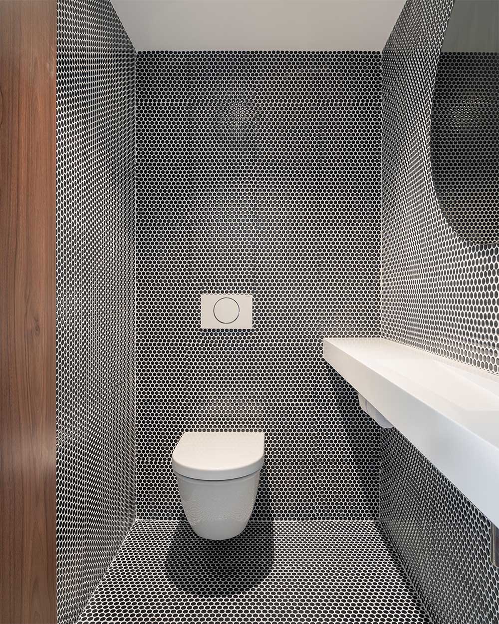 A modern powder room that has black penny tiles with white grout that cover the walls and floor.