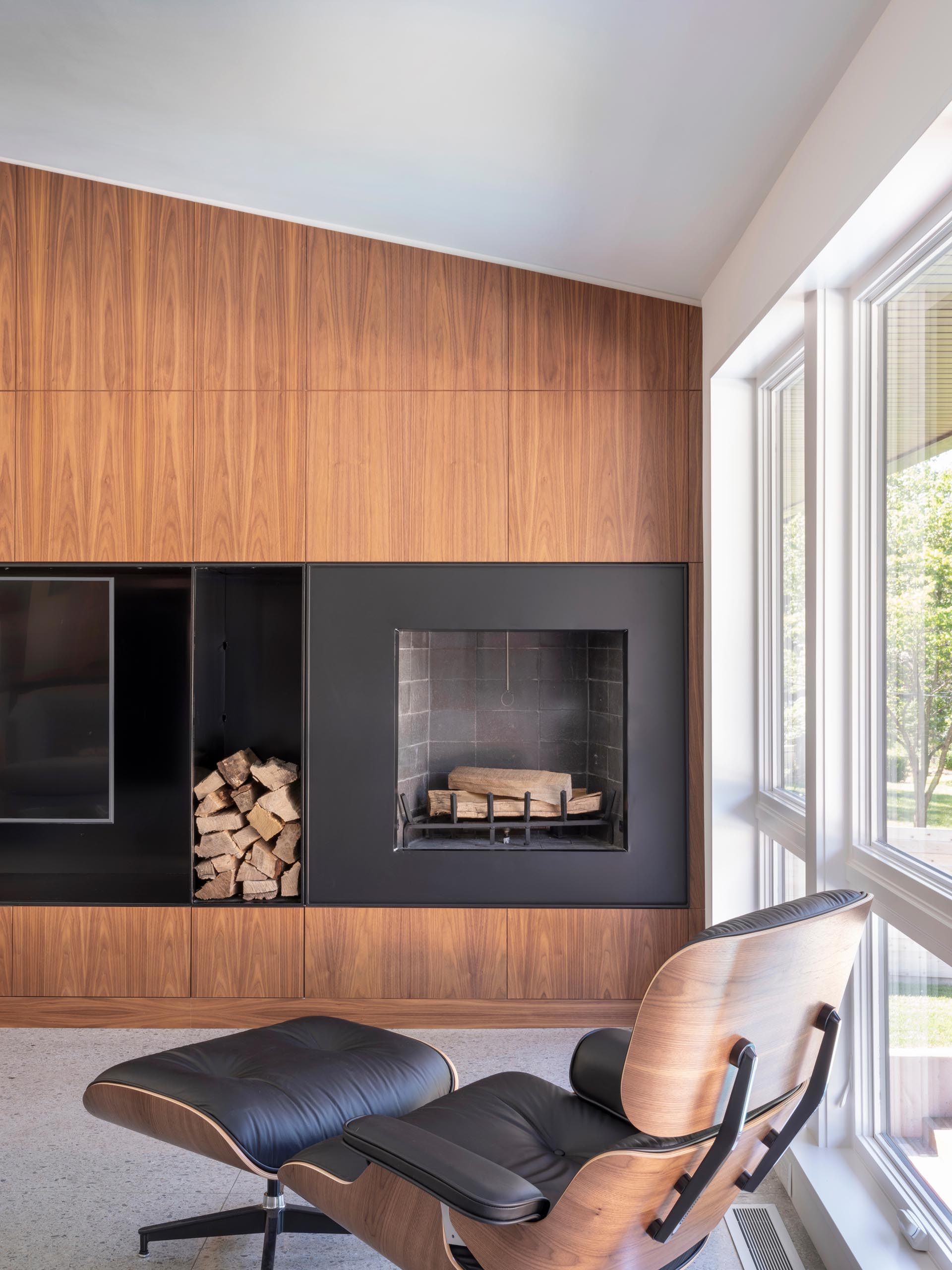 A modern living room with a wood accent wall that's split by the inclusion of black steel, which houses the television and fireplace.