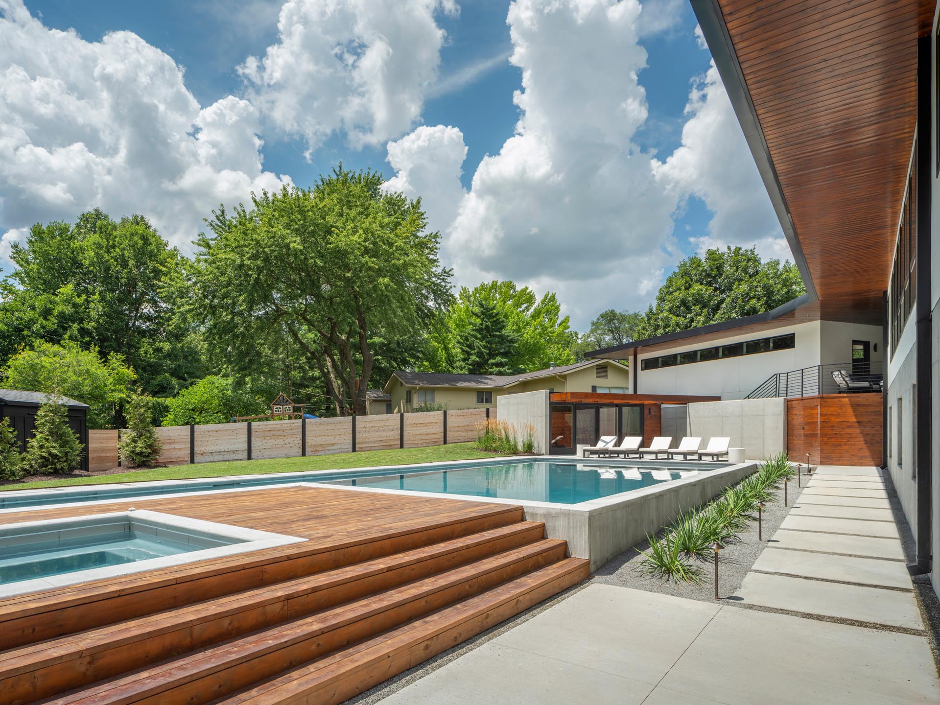 A mid-century modern inspired home with large landscaped yard, a swimming pool with a hot tub, a pool house, outdoor shower, and a deck.