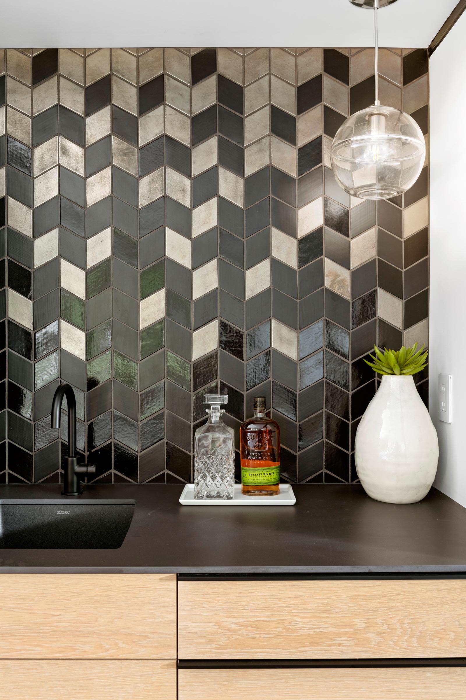 A modern bar area with a matte and glossy tiled wall that matches the black countertop.