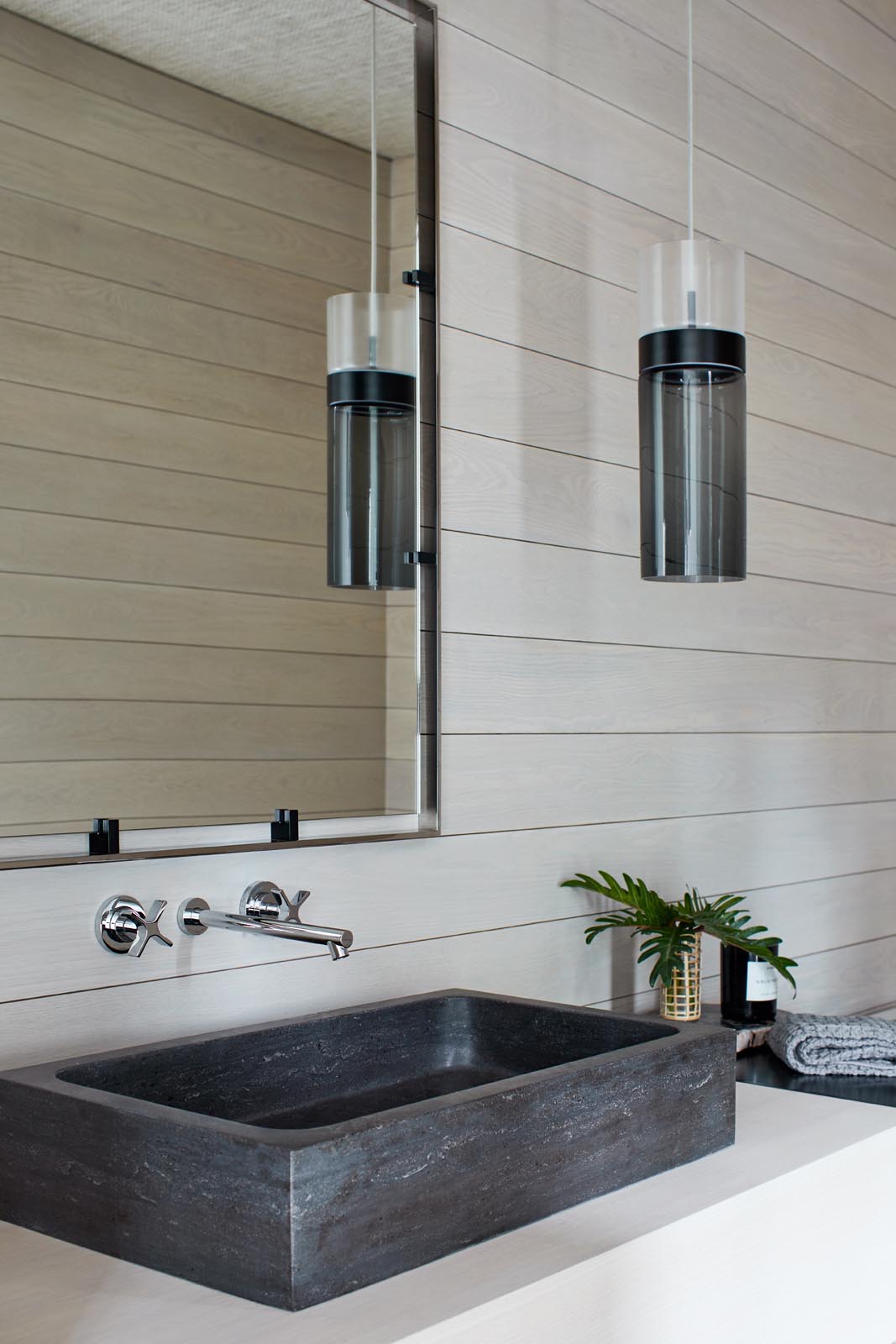 A modern bathroom with light wood walls that are contrasted by a black pendant light and sink.