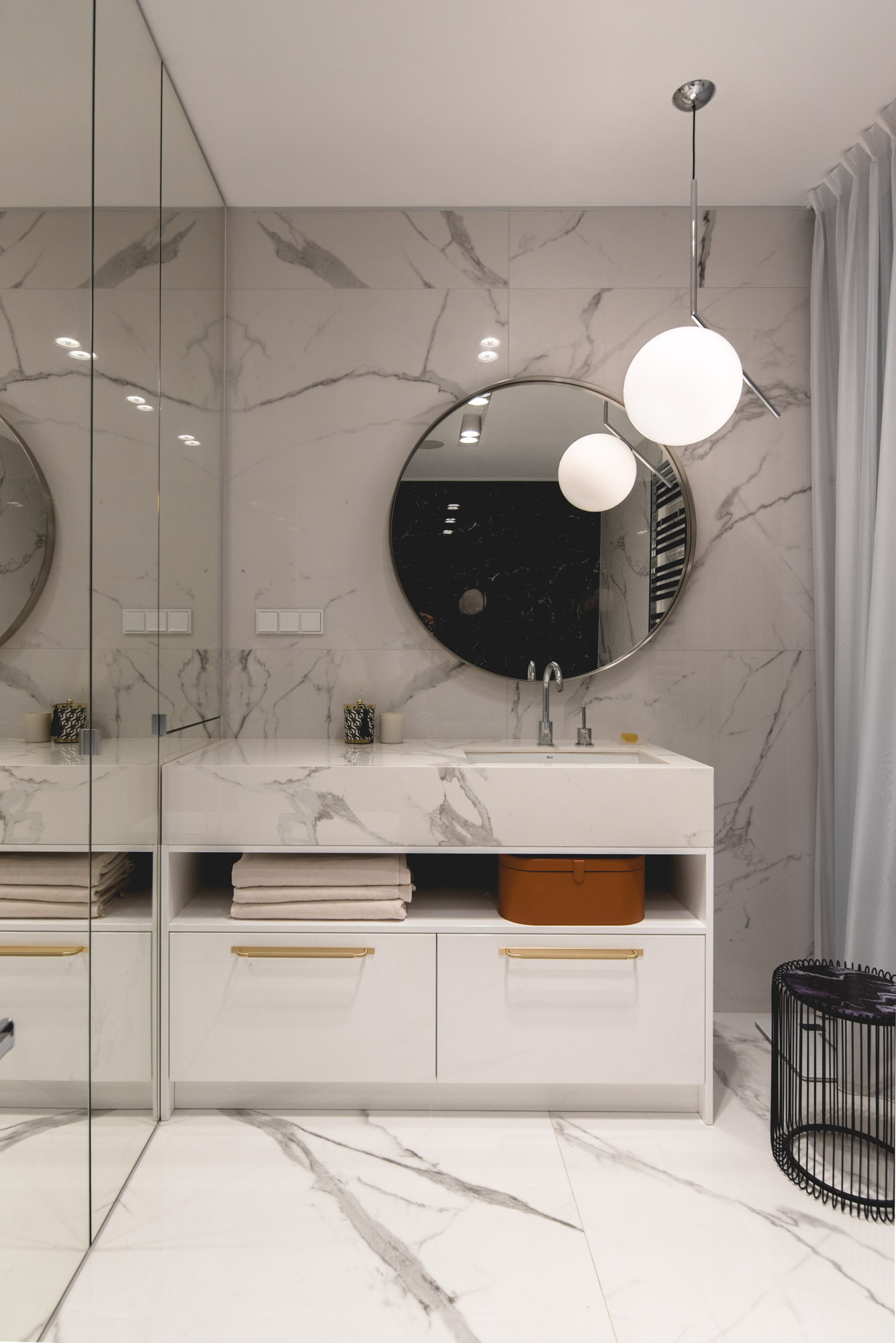 In this modern bathroom, stone covers the walls and the vanity, while the round mirror and pendant light add a curved element.