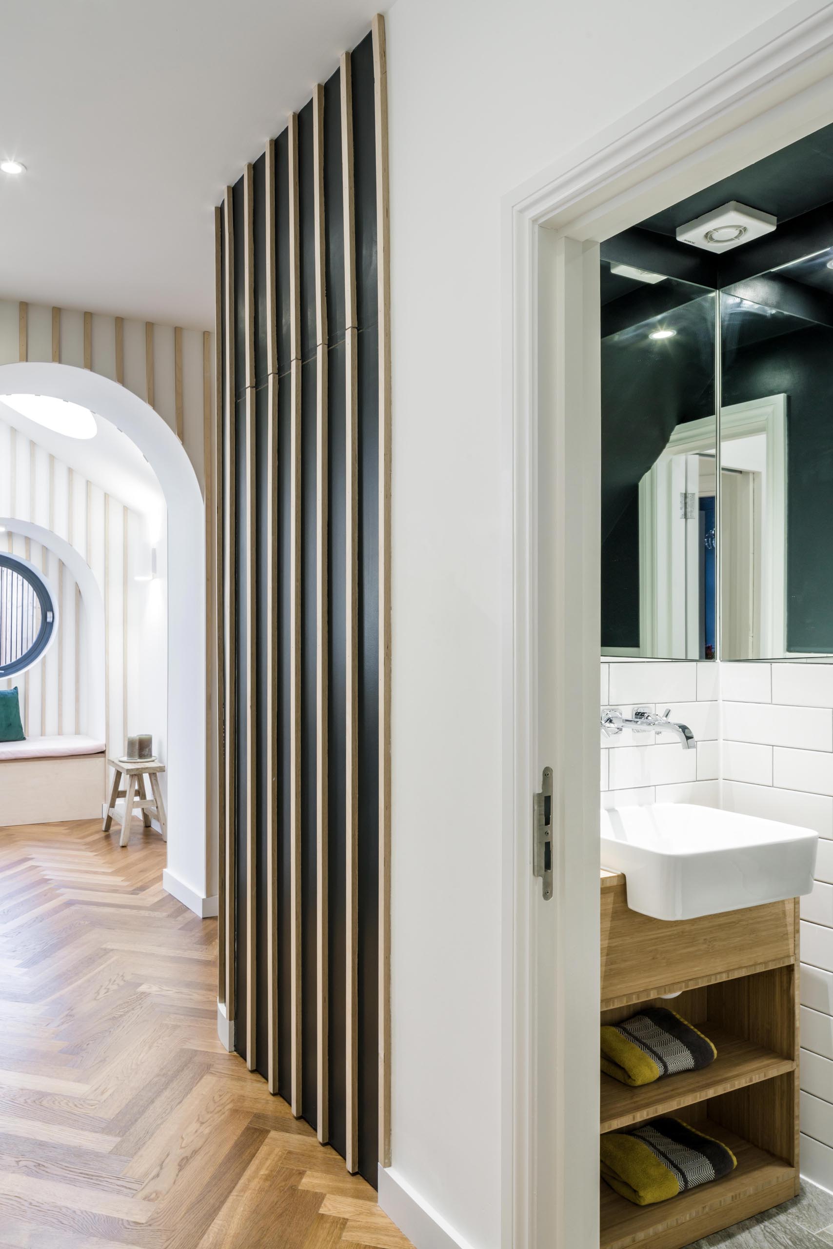 A small powder room that includes a dark ceiling, mirrors that the line the corner, a wood vanity, and white tiles.