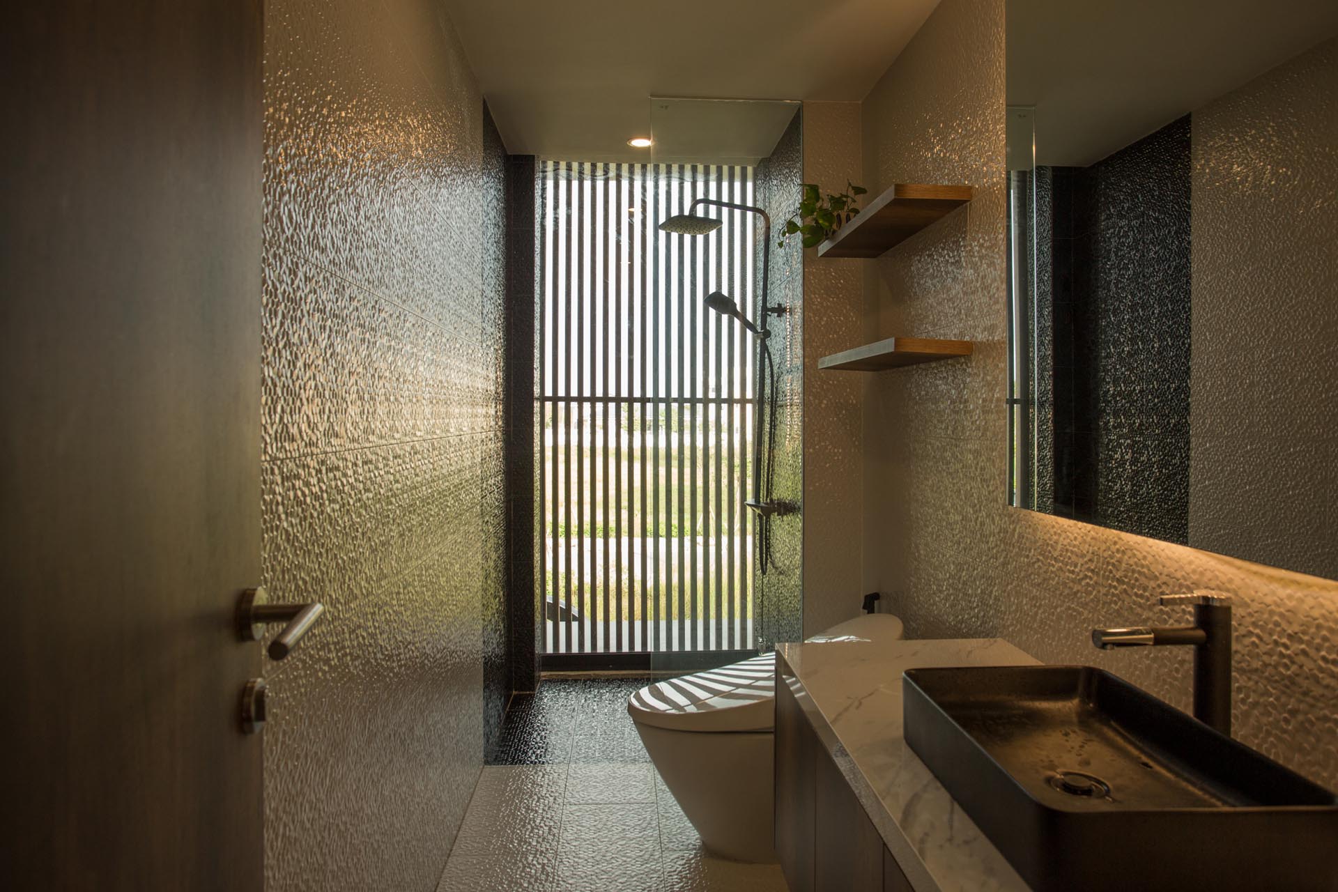 In a modern bathroom, textured tiles cover the walls and floor, while the shower is located by the window providing views of the outdoors.