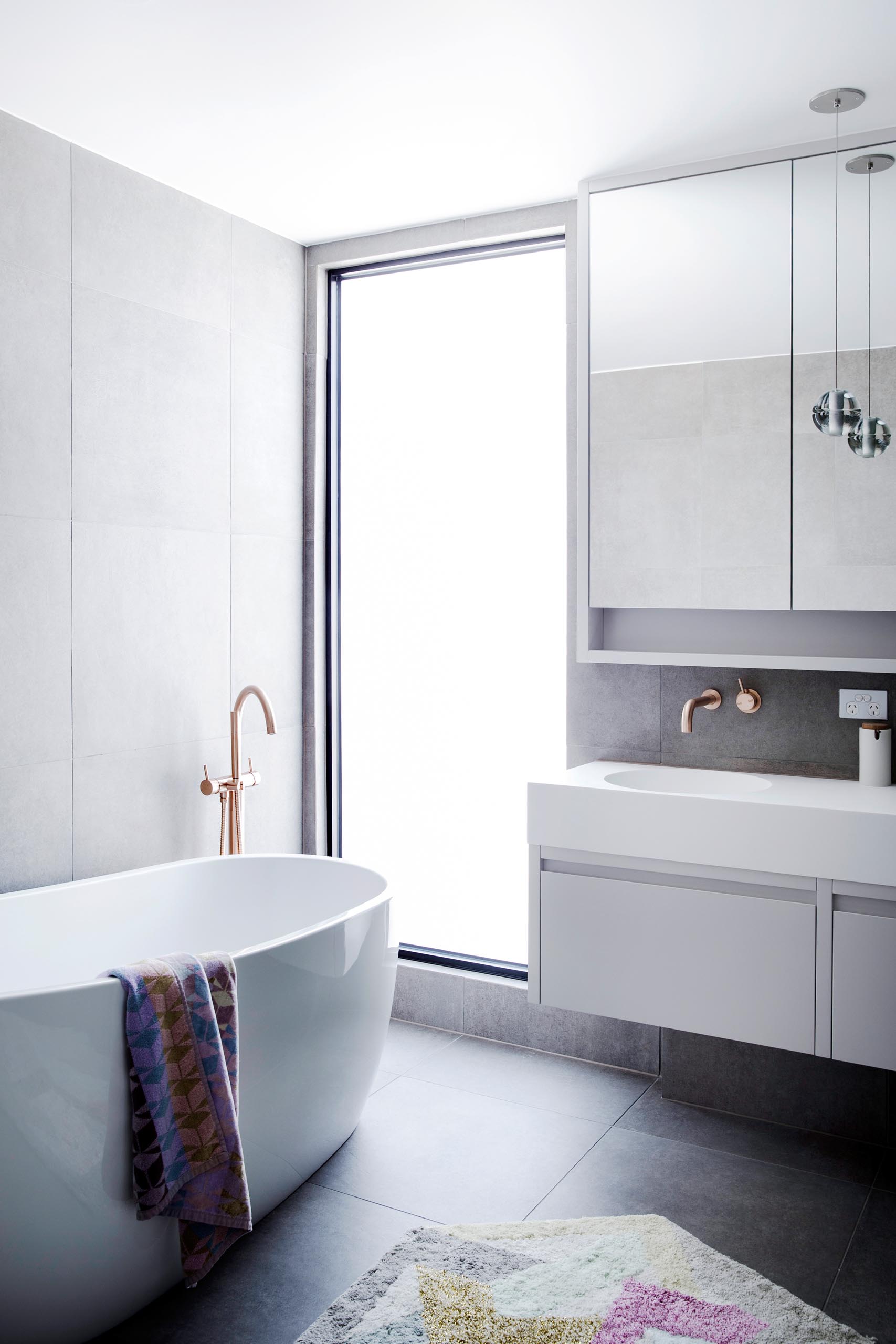 A modern bathroom with a large vertical window that floods the freestanding bathtub with natural light.