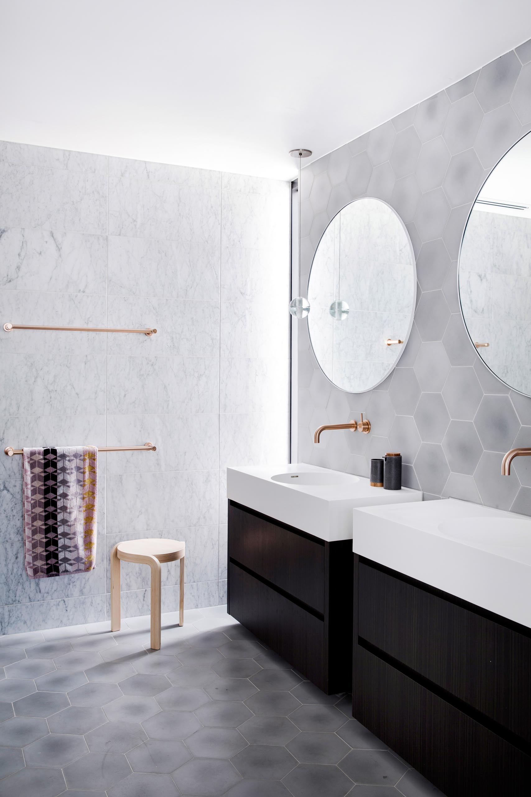 Stepping inside this master bathroom, natural light from the tall narrow window in the corner highlights the brushed rose gold towel bars mounted to the wall, that's covered with large format tiles. 