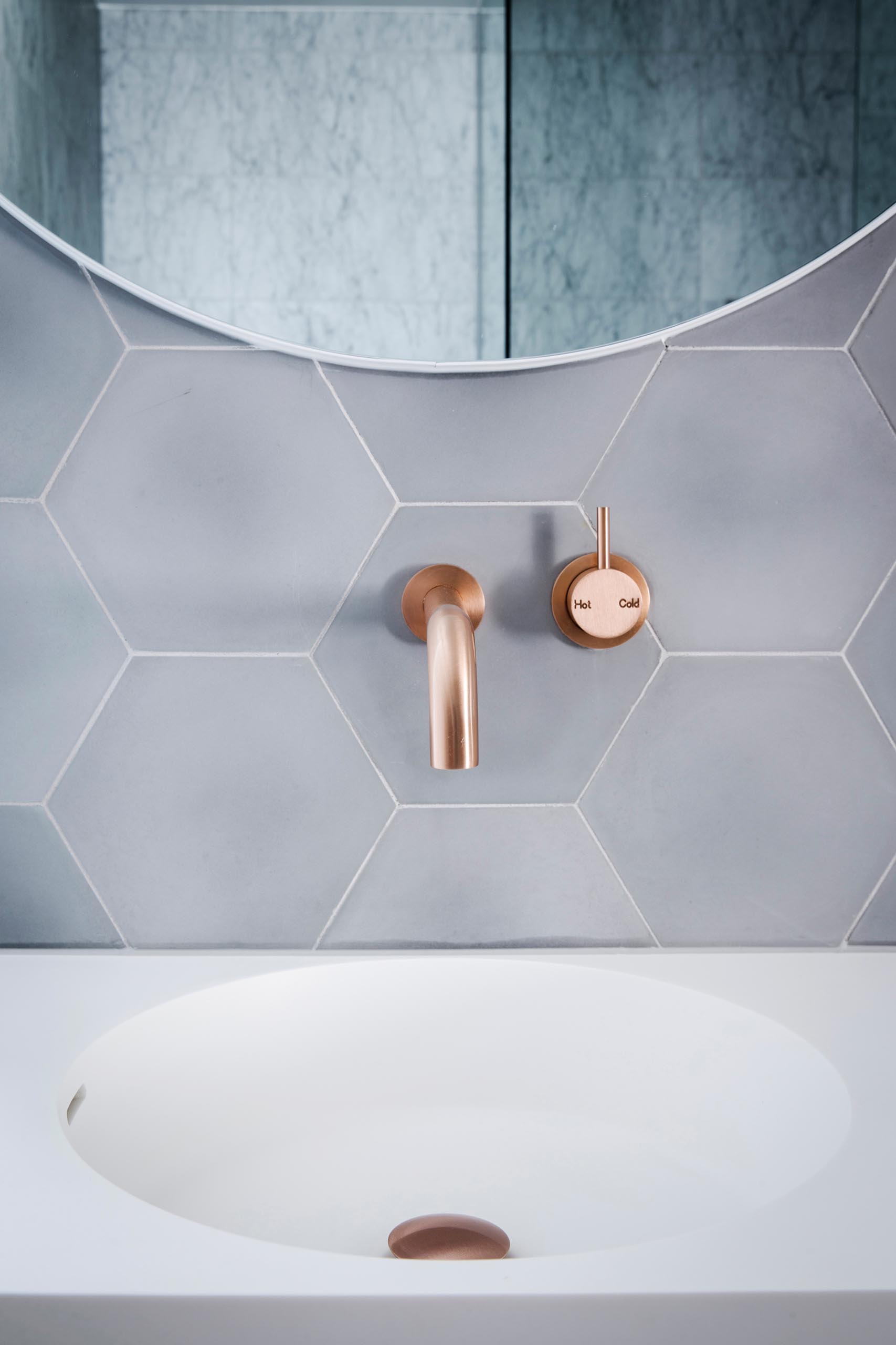 Hexagonal grey tiles with thin white grout provide a backdrop for the brushed rose gold faucet and round mirrors.