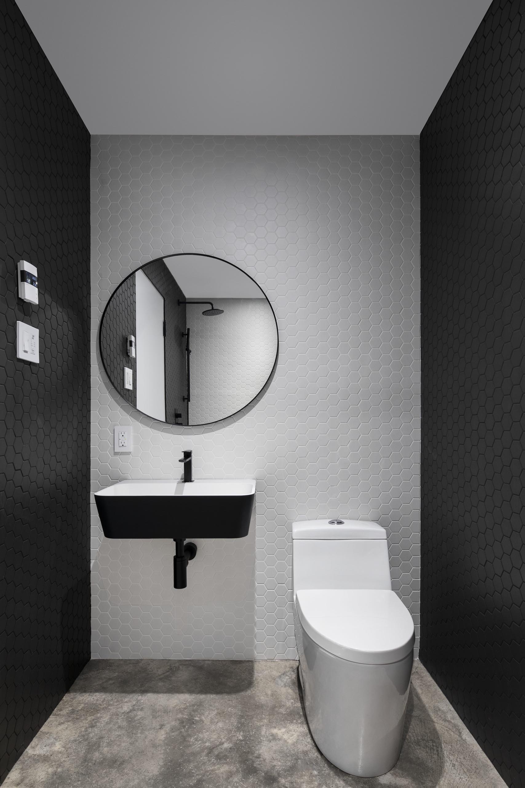 In this modern powder room, hexagonal black and white tiles cover the walls.