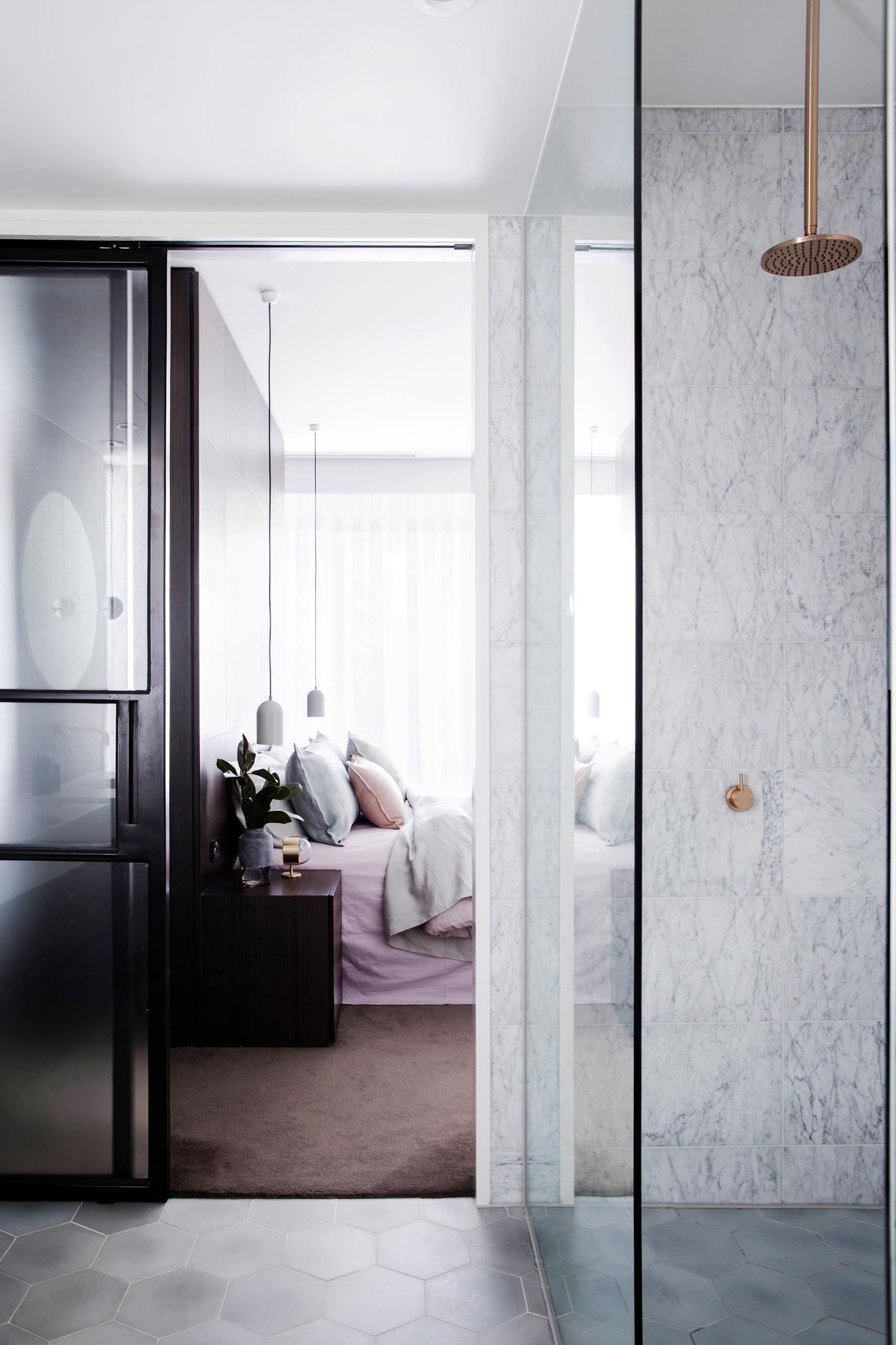 A modern shower with with a rainfall shower head and marble walls. The hexagonal tile used on the wall with the vanities, carries through to the floor and into the shower.