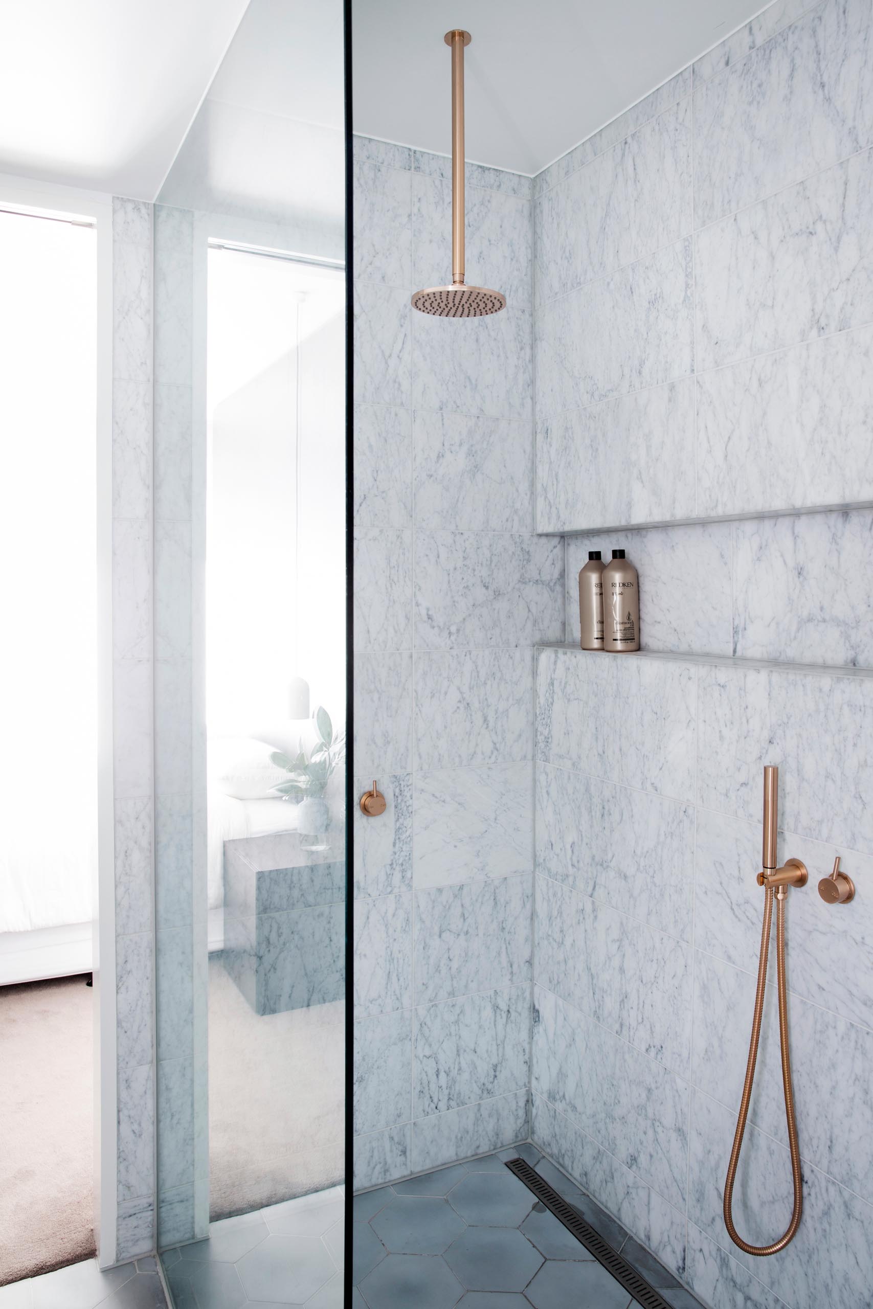 A modern gray marble shower with a rainfall shower head, brushed rose gold hardware, and a built-in shower niche.