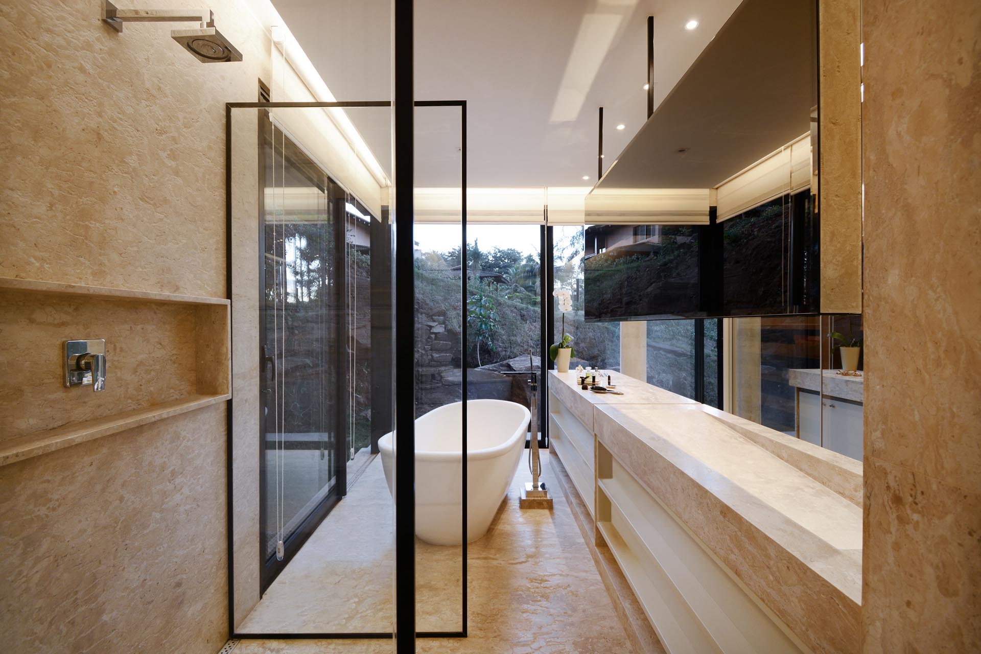 A modern bathroom with floor-to-ceiling windows that provide tree views for the freestanding bathtub.