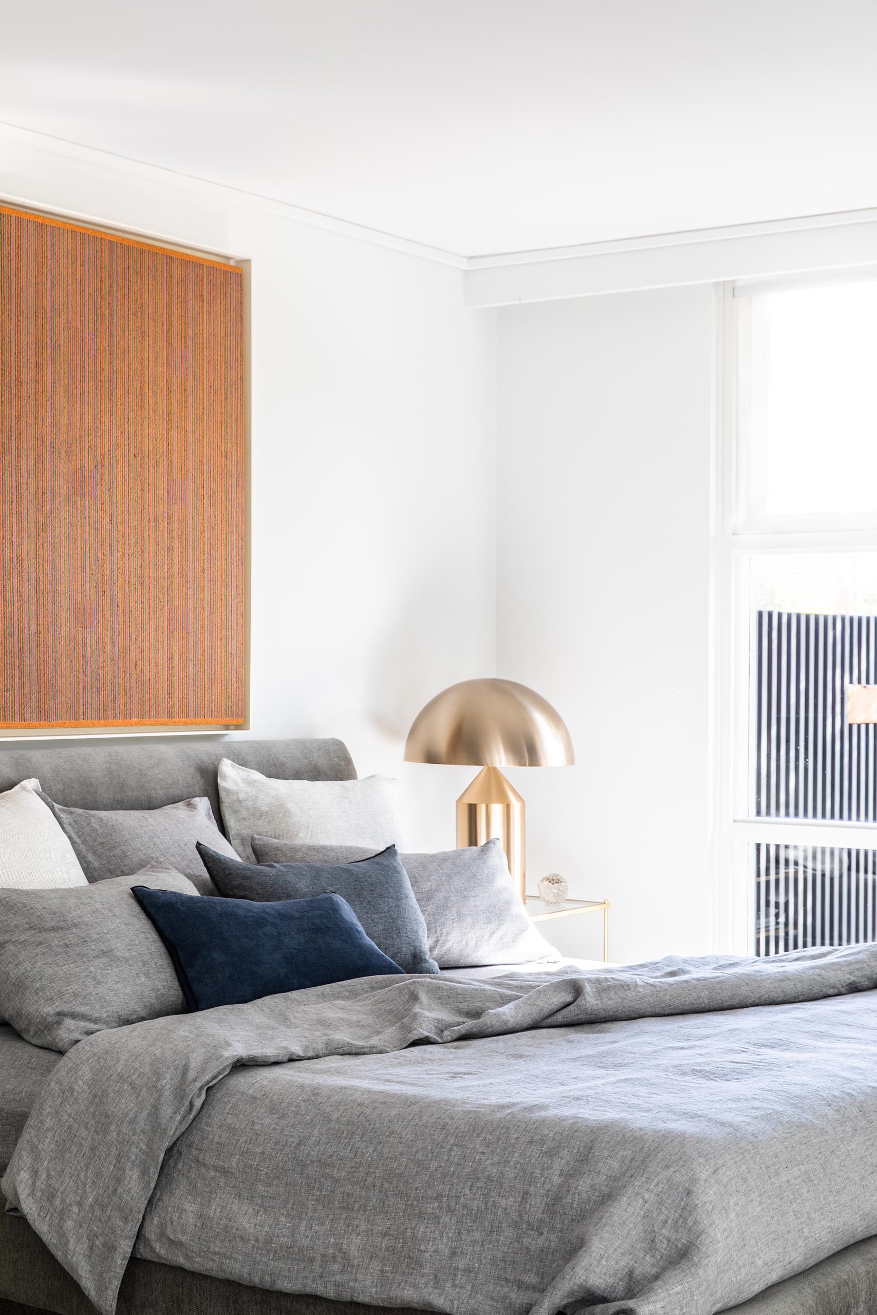 In this modern bedroom, an art piece and gray bedding adds color to the room, while the metallic accents add a touch of glamour.