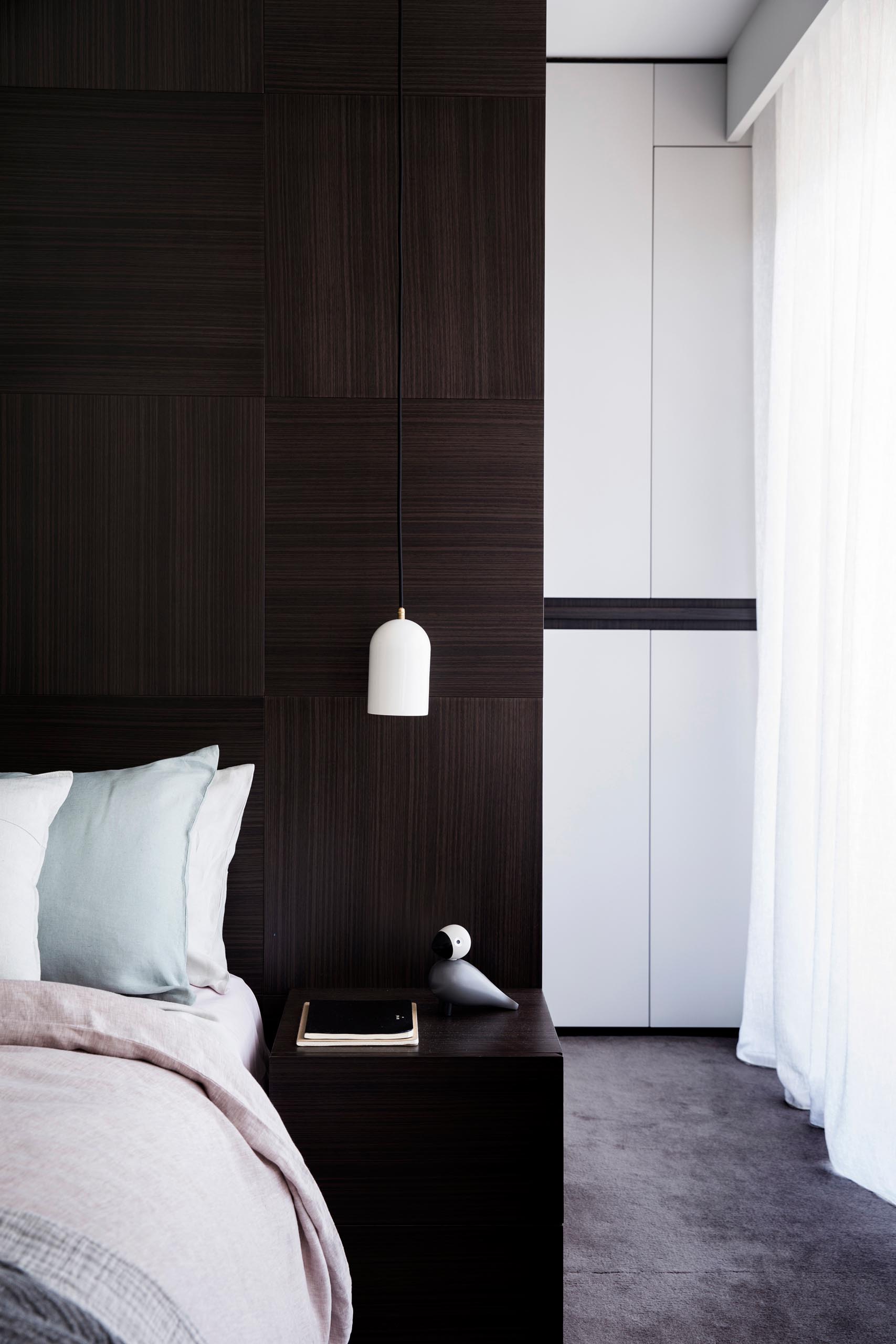 A modern master bedroom with a dark wood accent wall and a walk-through closet.