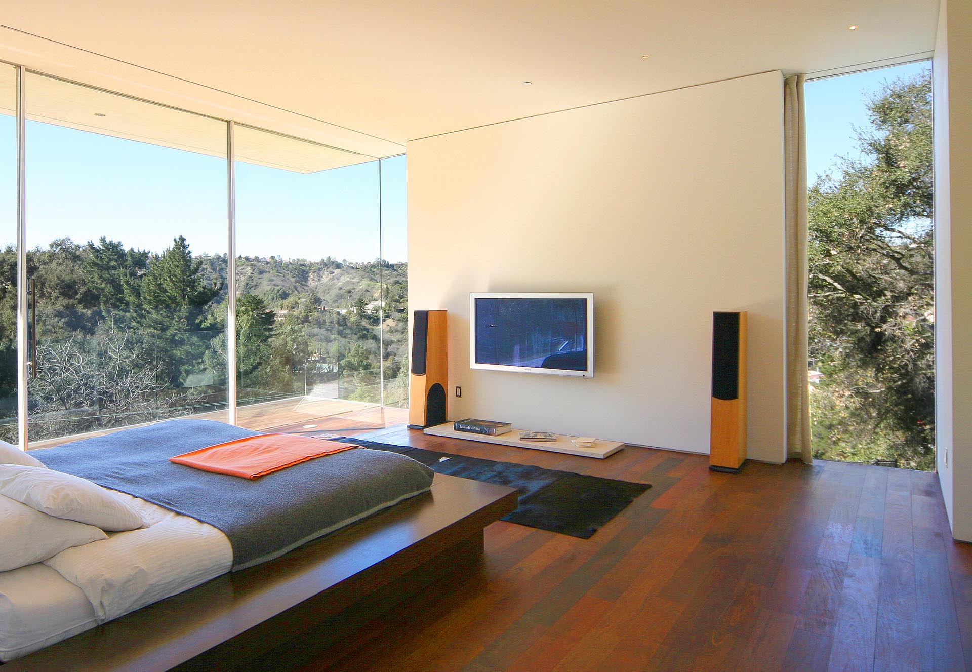 A master bedroom with natural stucco walls, floor to ceiling windows, and Brazilian walnut floors.