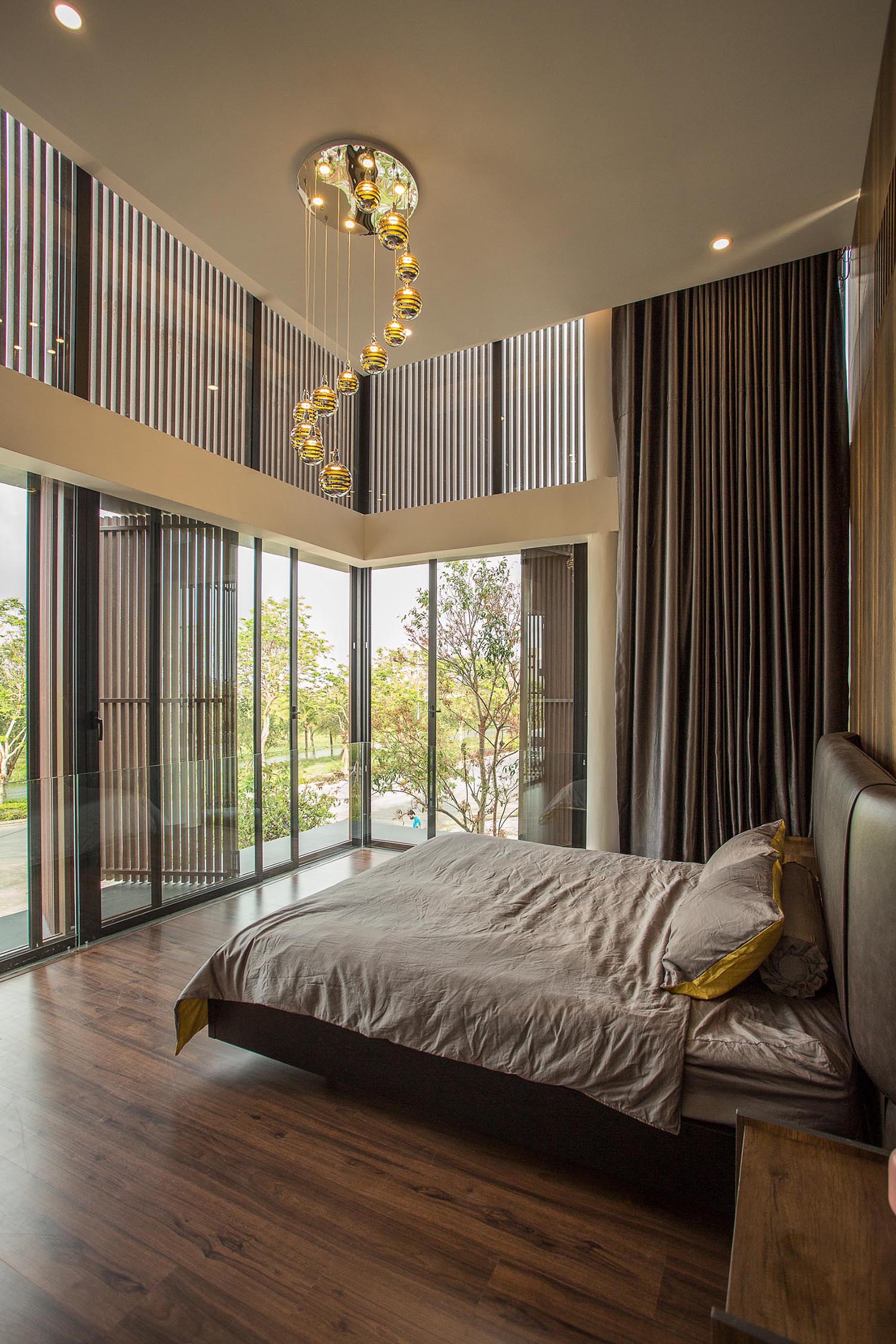 In a modern bedroom, the high ceiling allows for a grand appearance, while a wood accent wall has strips of LED lights that run from the ceiling to the floor.