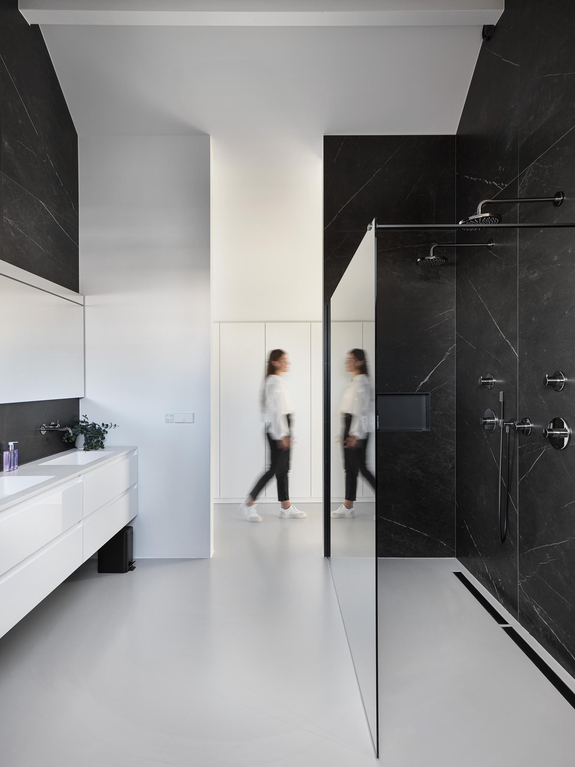 In this modern bathroom, there's black stone on the walls that provides a contrasting element to the white vanity.