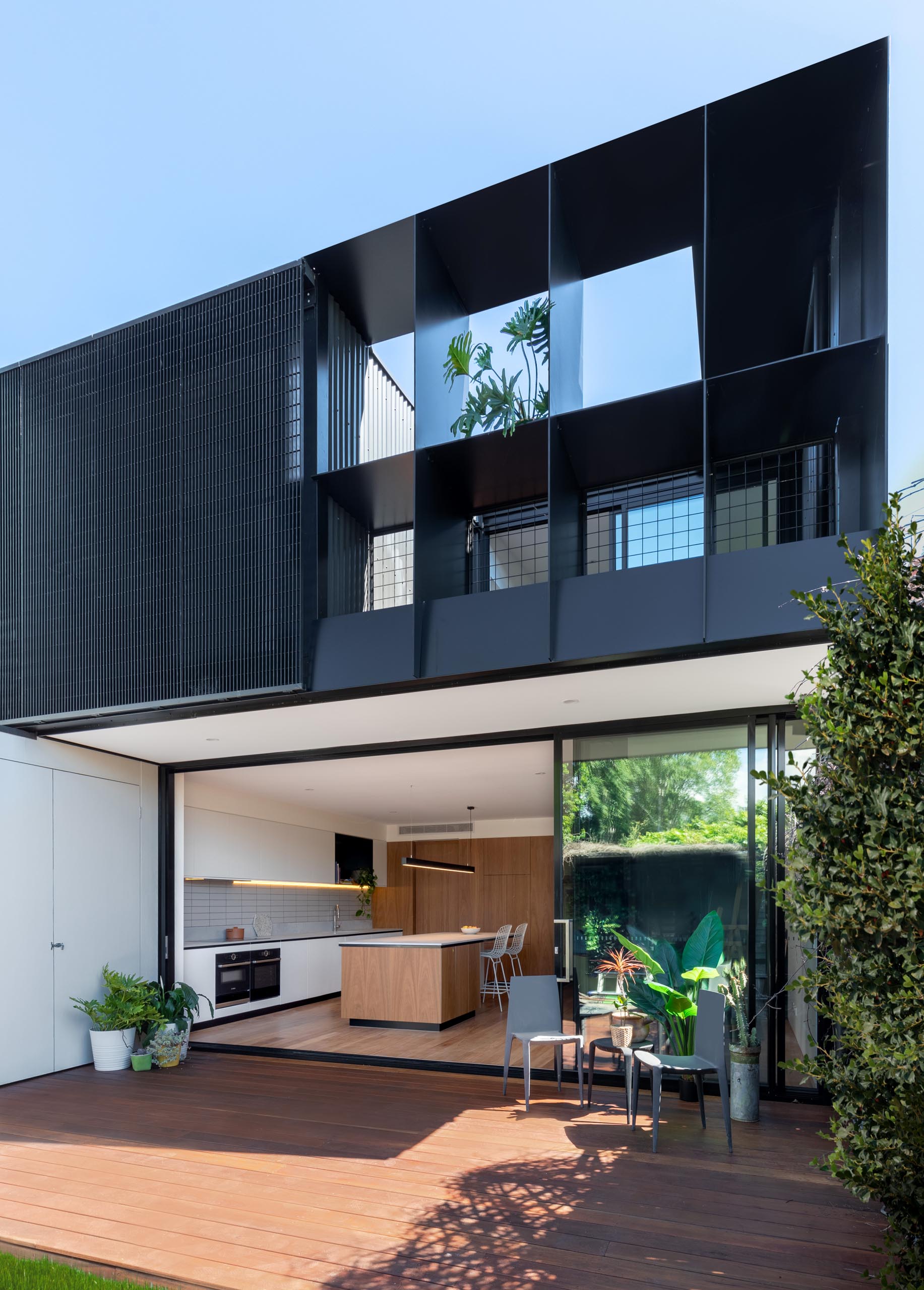 A modern house extension with a sliding glass wall that opens to the backyard, which provides a view of the rear dark gray corrugated metal addition.