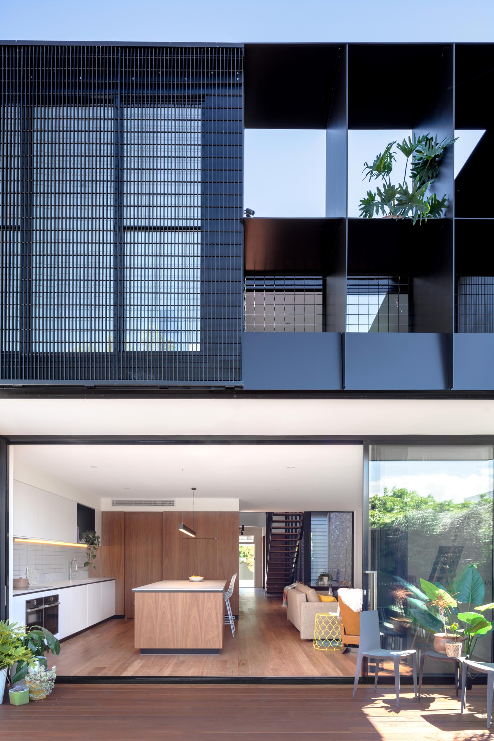 A modern house extension with a sliding glass wall that opens to the backyard, which provides a view of the rear dark gray corrugated metal addition.