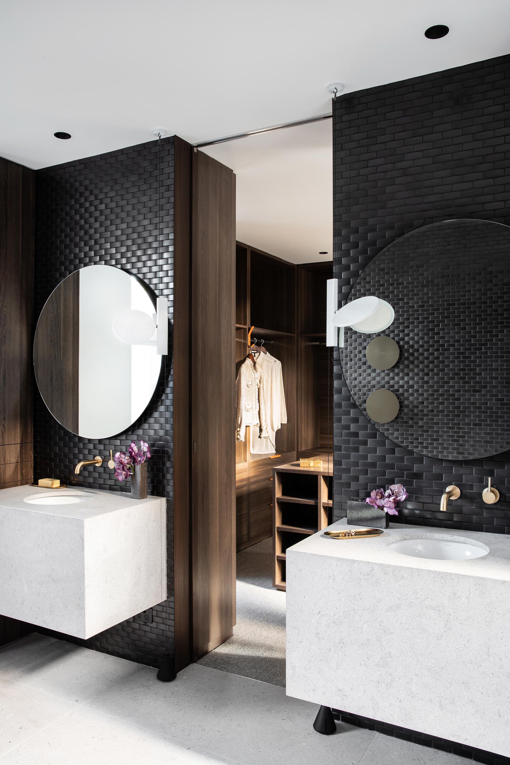 In the master bathroom, black tiles cover walls, while round mirrors hang above white vanities with undermount sinks.