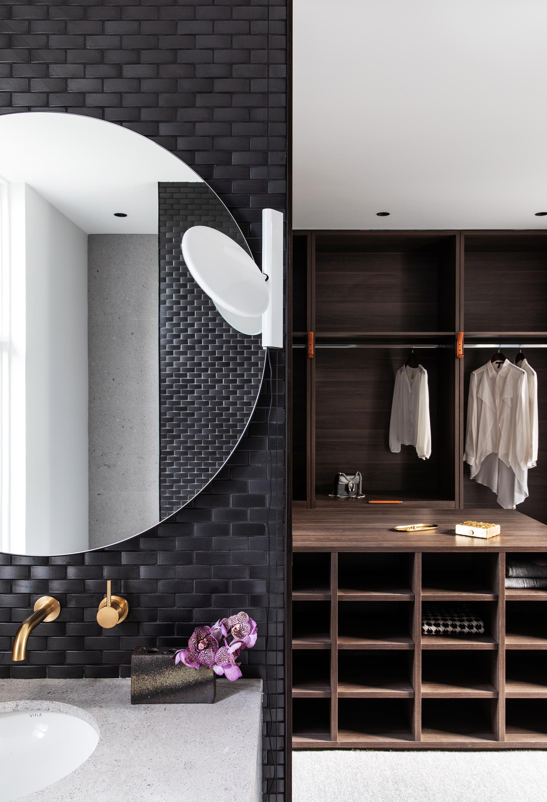 In the master bathroom, black tiles cover walls, while round mirrors hang above white vanities with undermount sinks. There's also a walk-in closet with dark wood cabinetry.