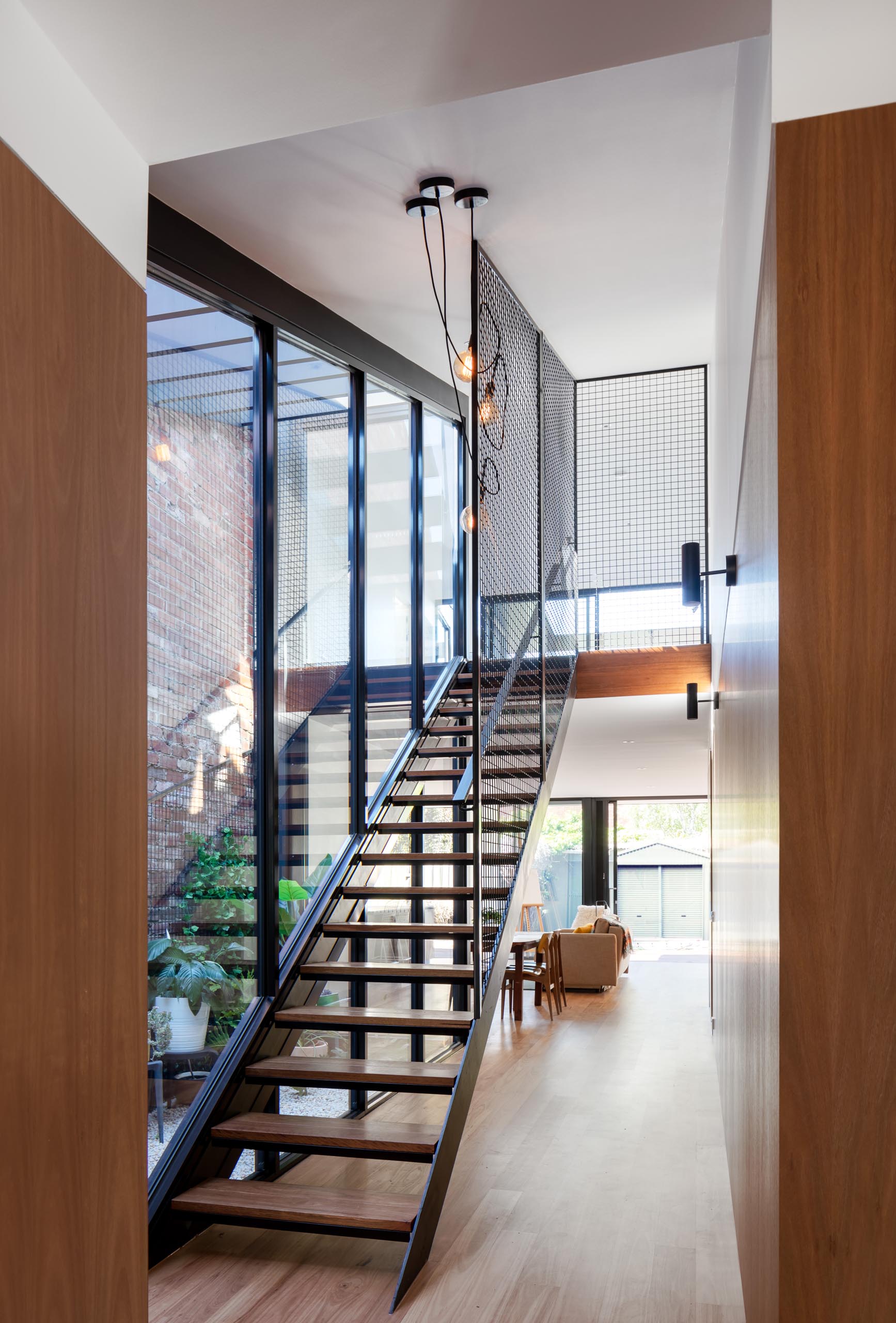 A modern wood and steel staircase that runs alongside a wall of glass.