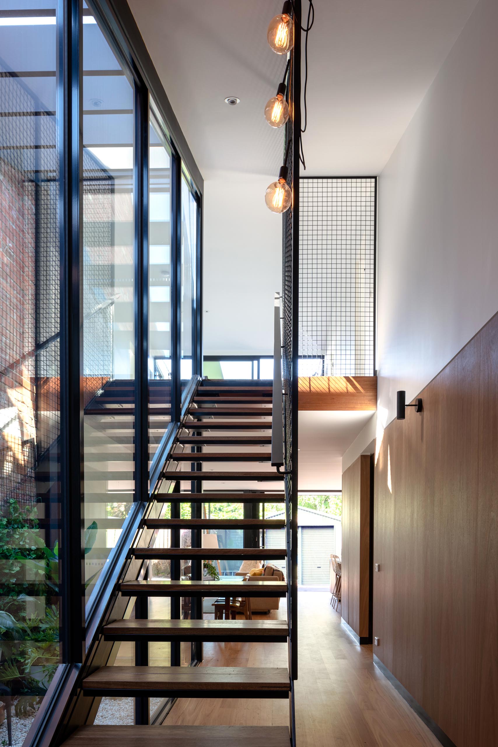 A modern wood and steel staircase that runs alongside a wall of glass.