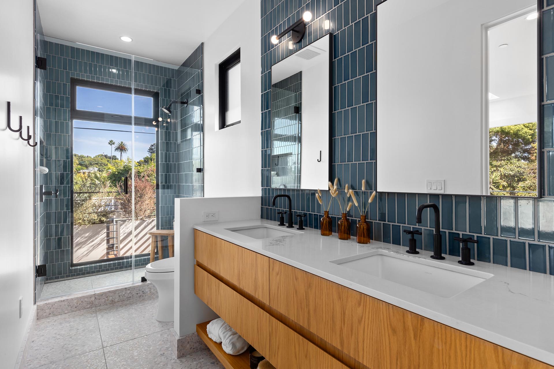 In this modern bathroom, blue tiles are featured on the wall and in the shower, and there's also a wood vanity with double sinks.