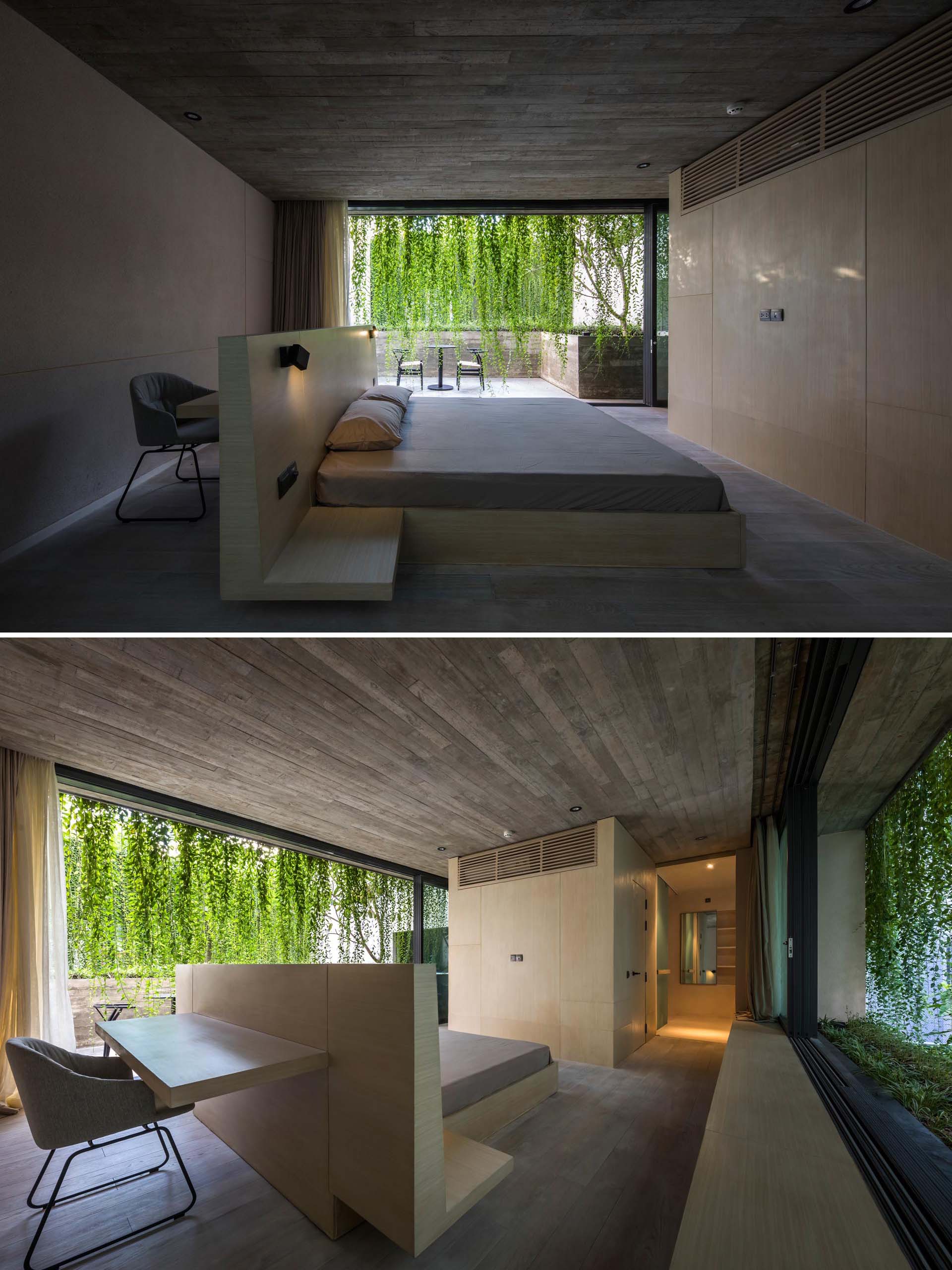 A minimalist bedroom with concrete walls, and a bed frame that incorporates a desk behind the headboard.