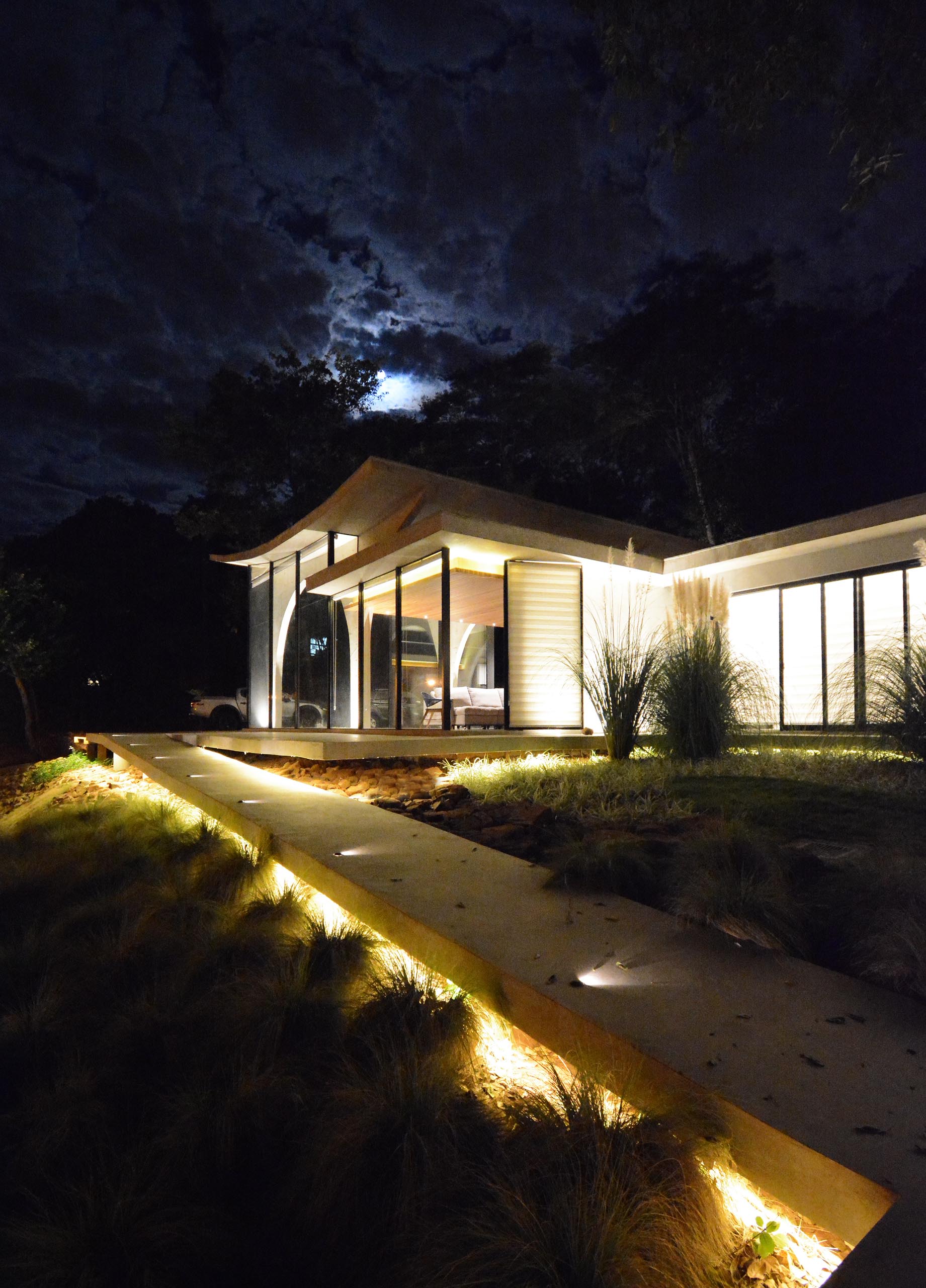 At the front of this modern home, there's a winding concrete path that's lit up at night, guiding people from the road up to the front door.