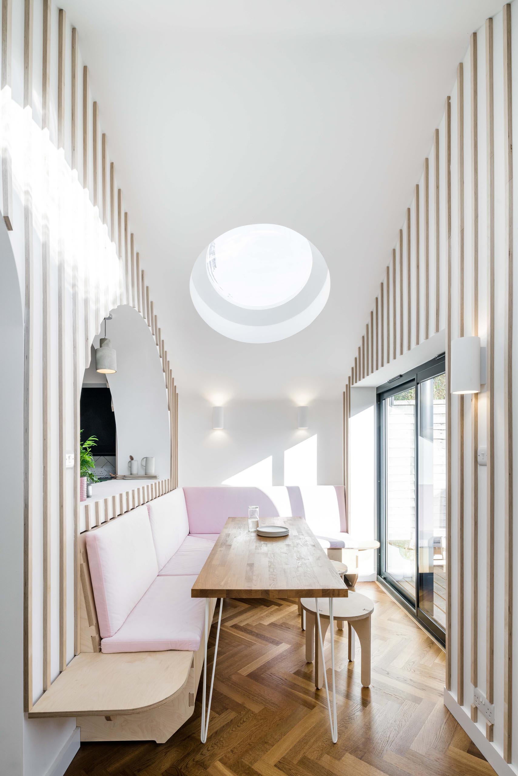 A modern dining area that has built-in banquettes that wrap around the corner of the space, while round skylights add a touch of natural light.