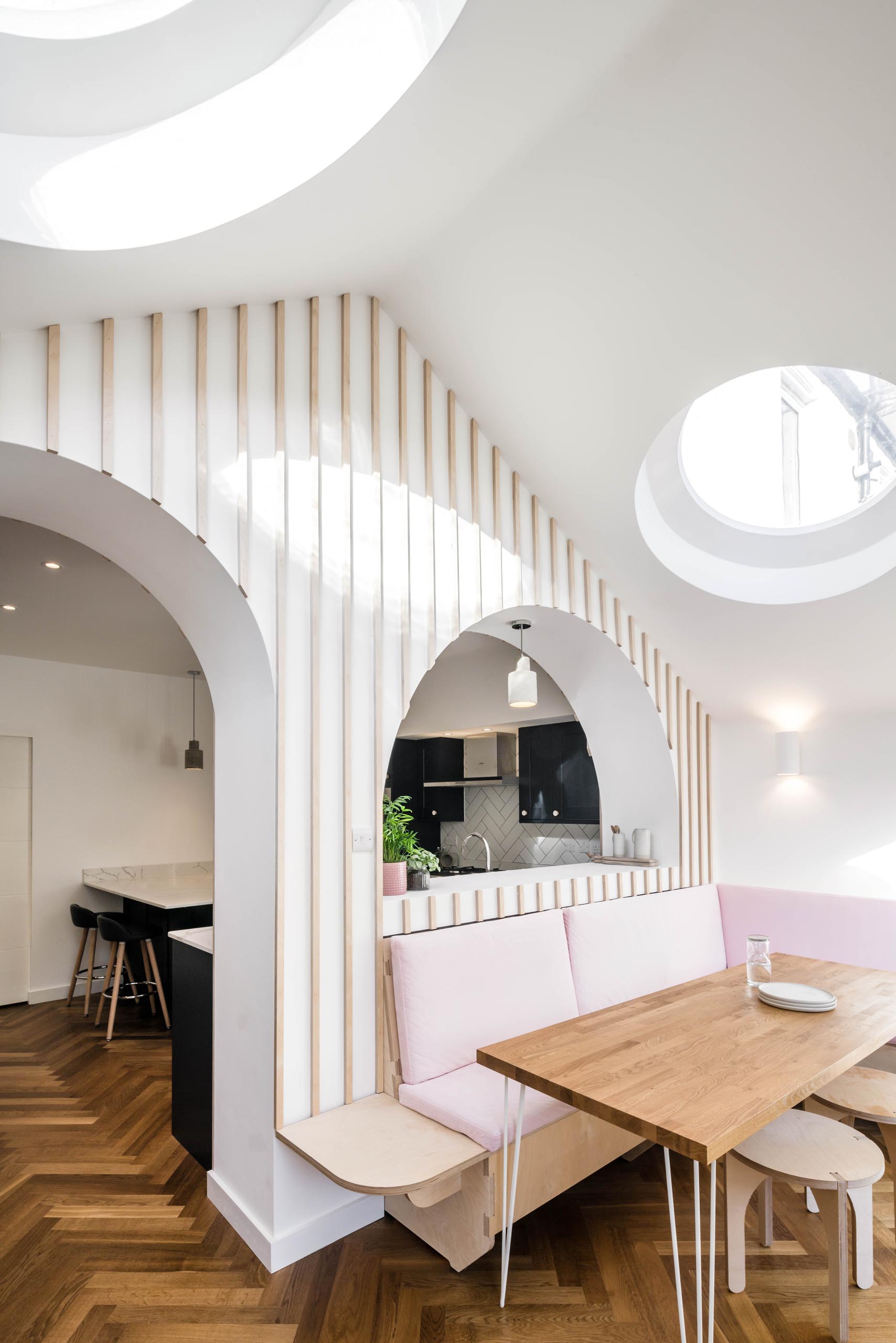 A modern dining area that has built-in banquettes that wrap around the corner of the space, while round skylights add a touch of natural light.