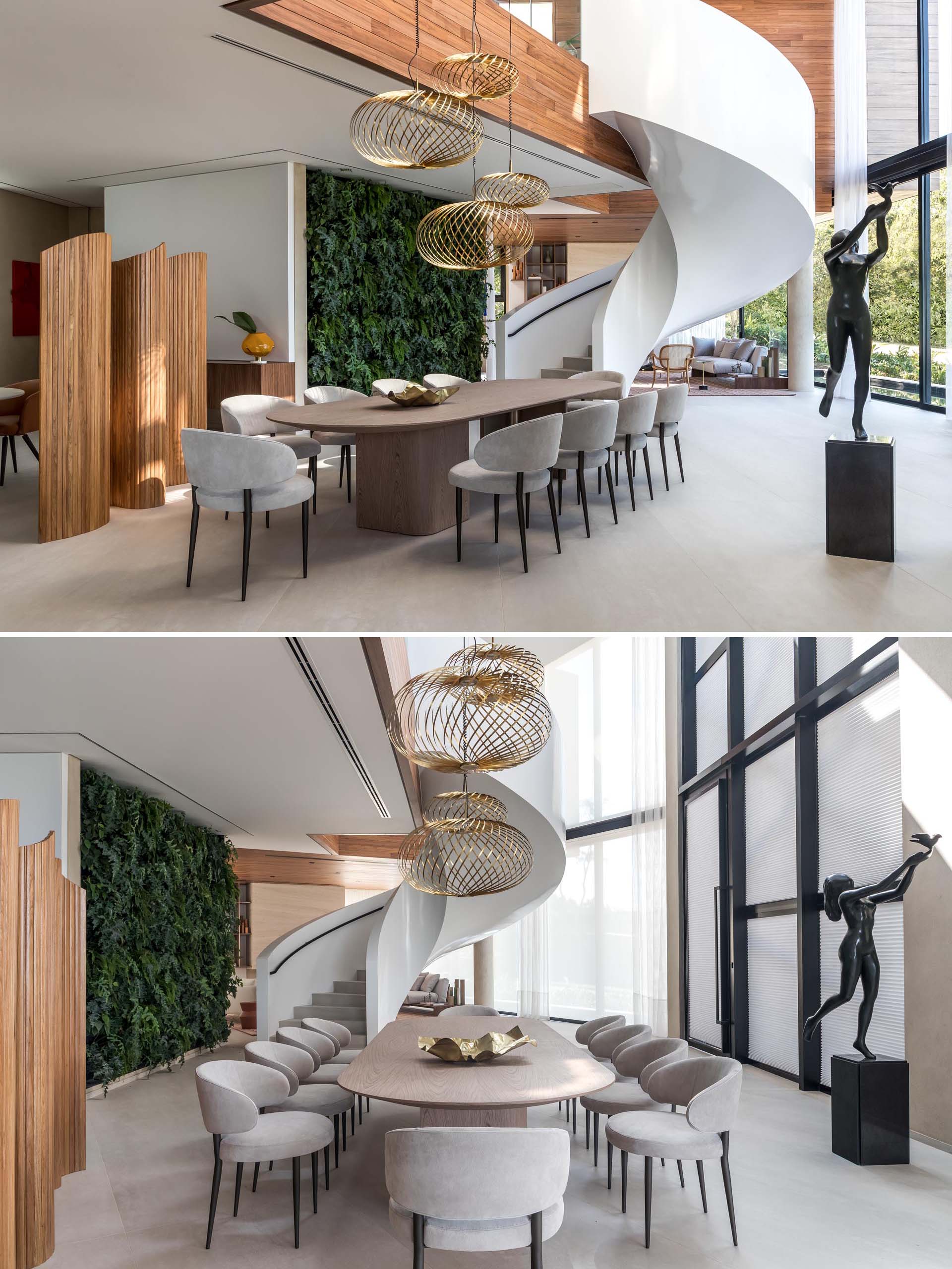 Sculptural metallic pendant lights hang above the rounded dining table in this modern dining room, while spiral stairs and a green wall separate the dining area from the living room.