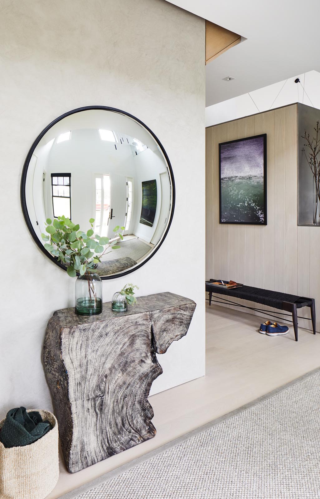 A modern entryway with a live edge wood console table and a round mirror with a black frame.