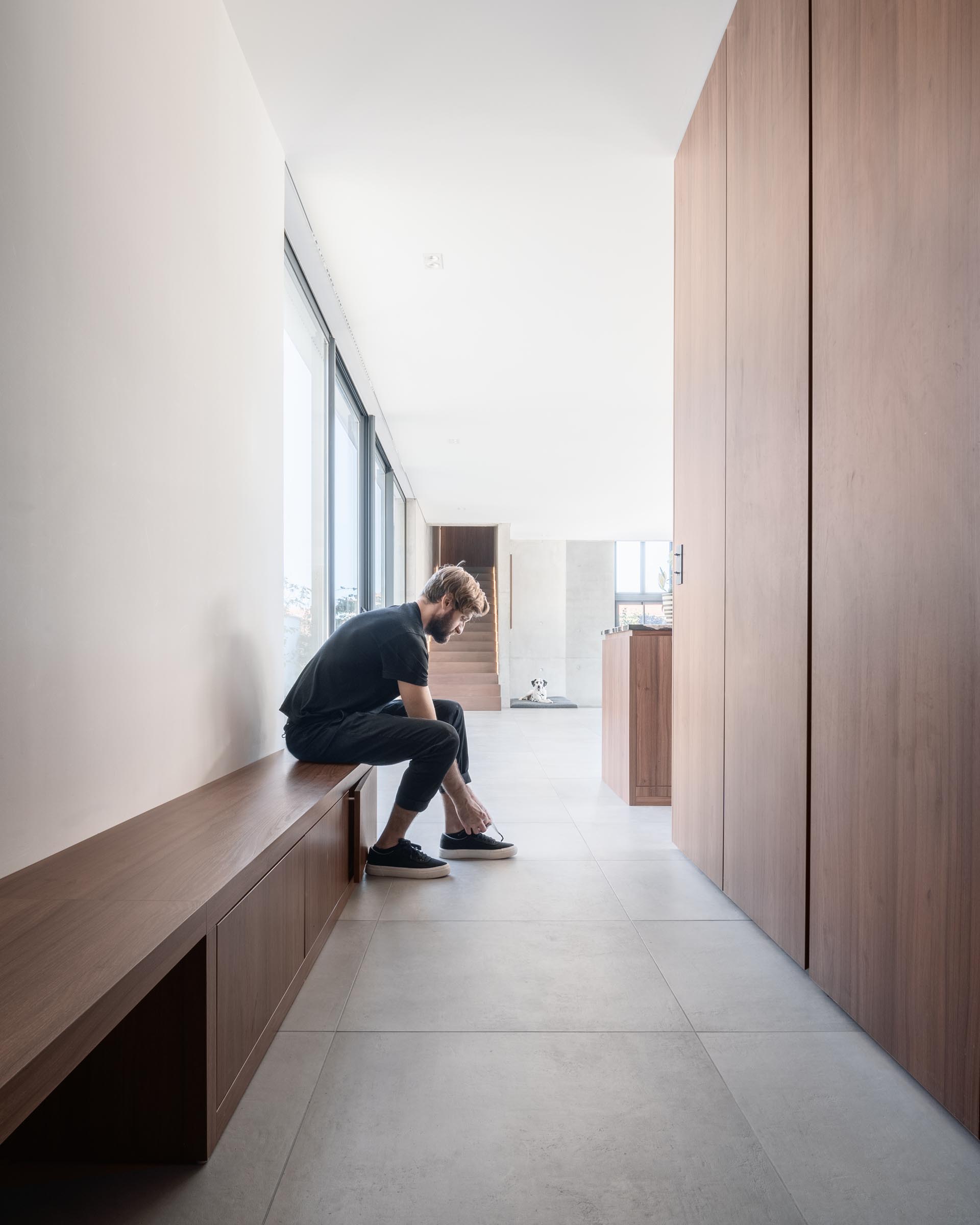 This modern entryway has a long wood bench, and on the opposite wall is a powder room and cabinets for storing jackets.